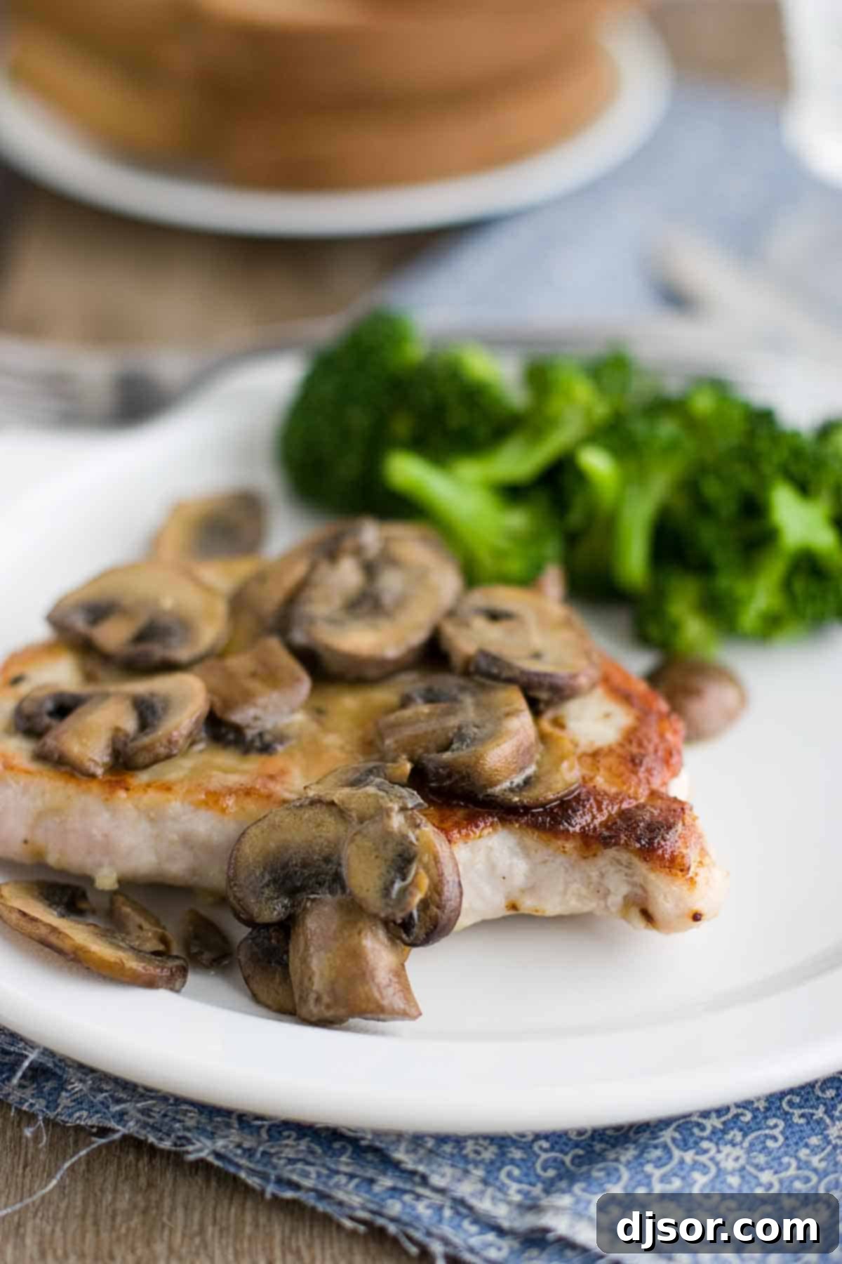 Seared Pork Chops with Tangy Dijon Mushrooms 2 Perfectly cooked pork chop covered in rich Dijon mushroom sauce, served alongside fresh broccoli on a white plate, ready for a quick and delicious dinner.