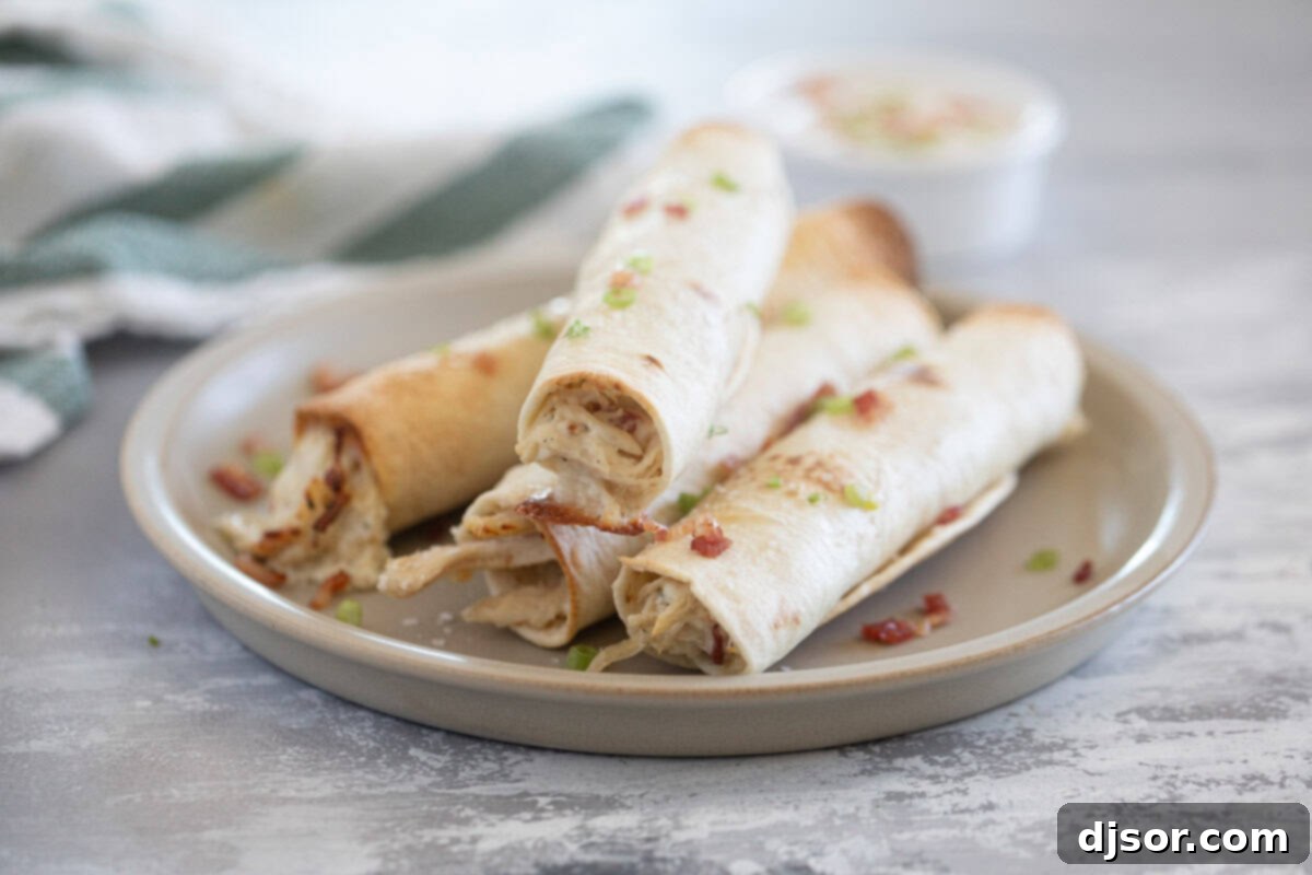 Four golden-brown Baked Chicken Bacon Ranch Taquitos served on a white plate, garnished with fresh sliced green onions and crumbled bacon.