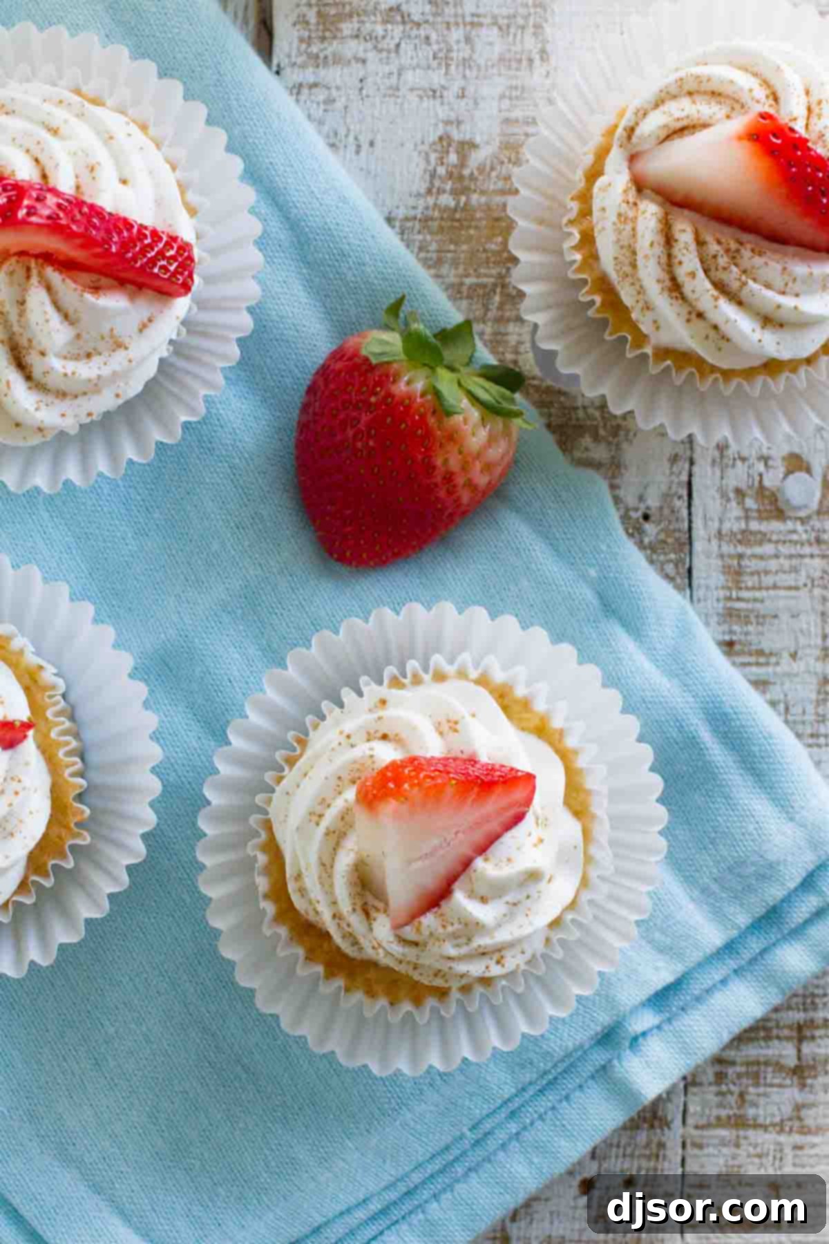 A trio of Tres Leches Cupcakes resting on a textured blue napkin, garnished with fresh strawberries, highlighting their moist texture and elegant presentation.