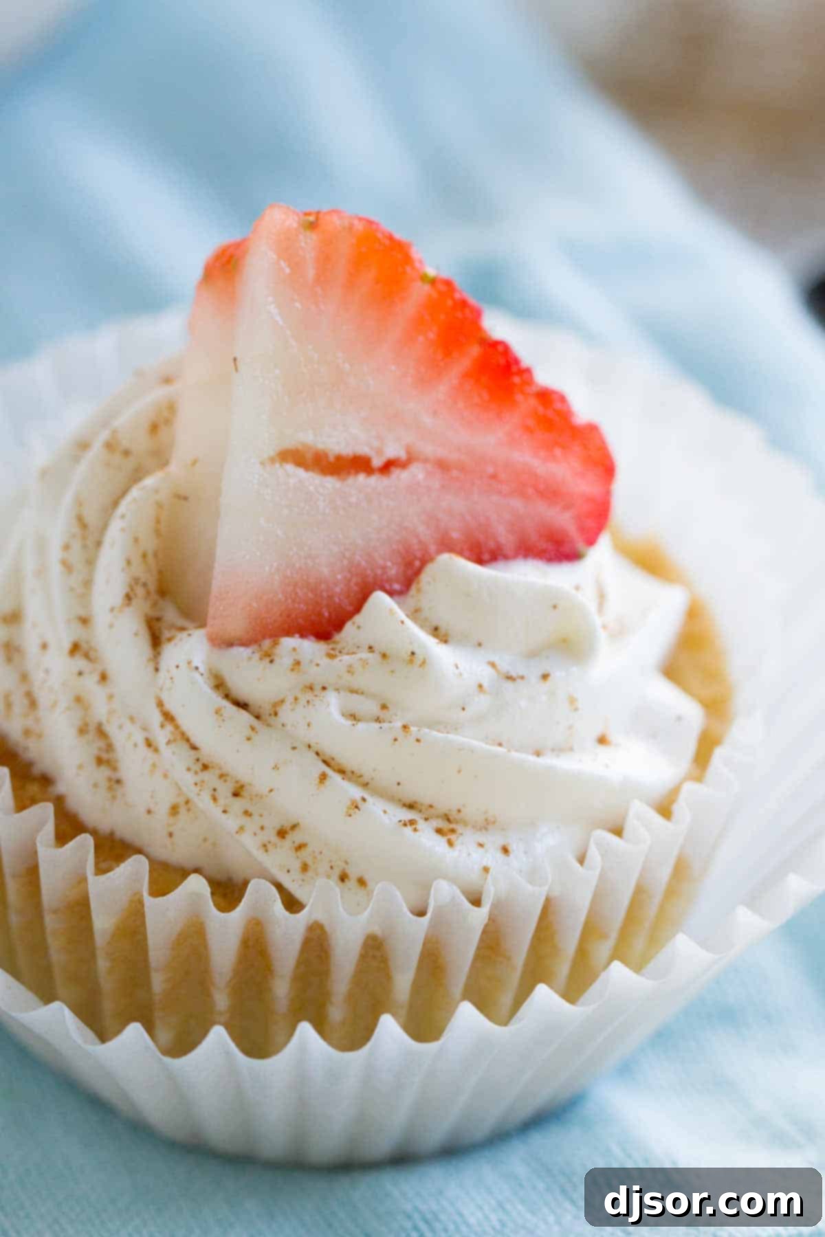 A single Tres Leches Cupcake with a generous swirl of whipped cream, dusted with cinnamon, and topped with a single strawberry slice, showcasing its irresistible appeal.
