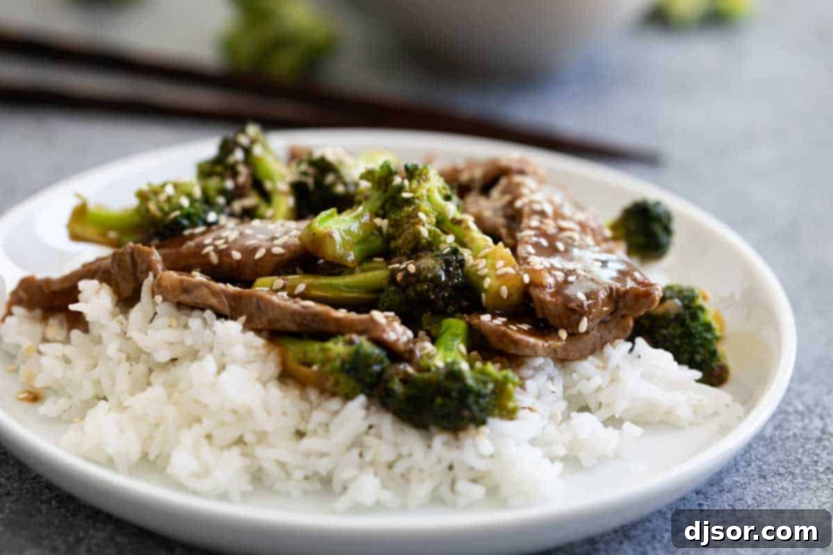 A plate of beef and broccoli served over white rice, garnished with sesame seeds.