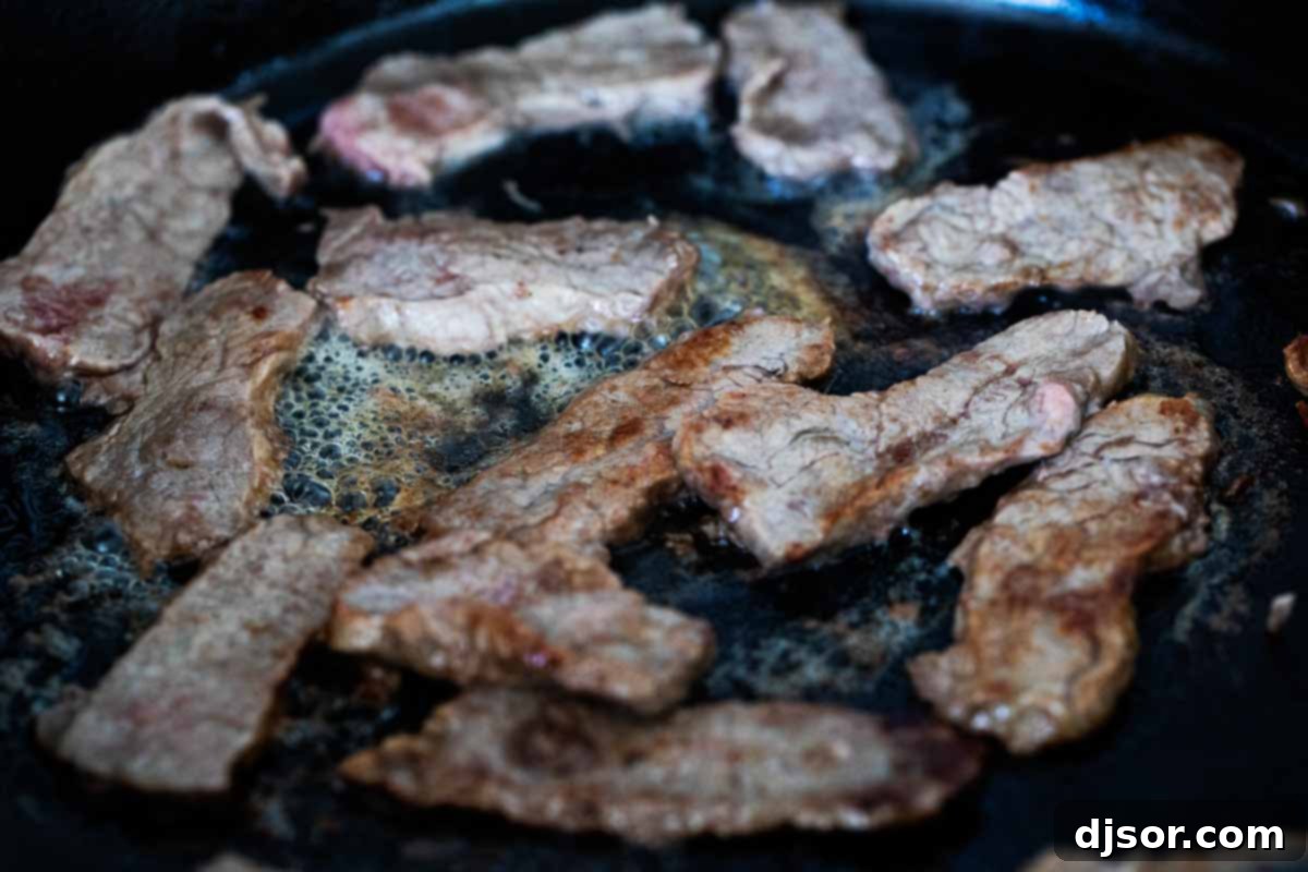 Thin strips of flank steak being seared in a hot cast iron skillet.