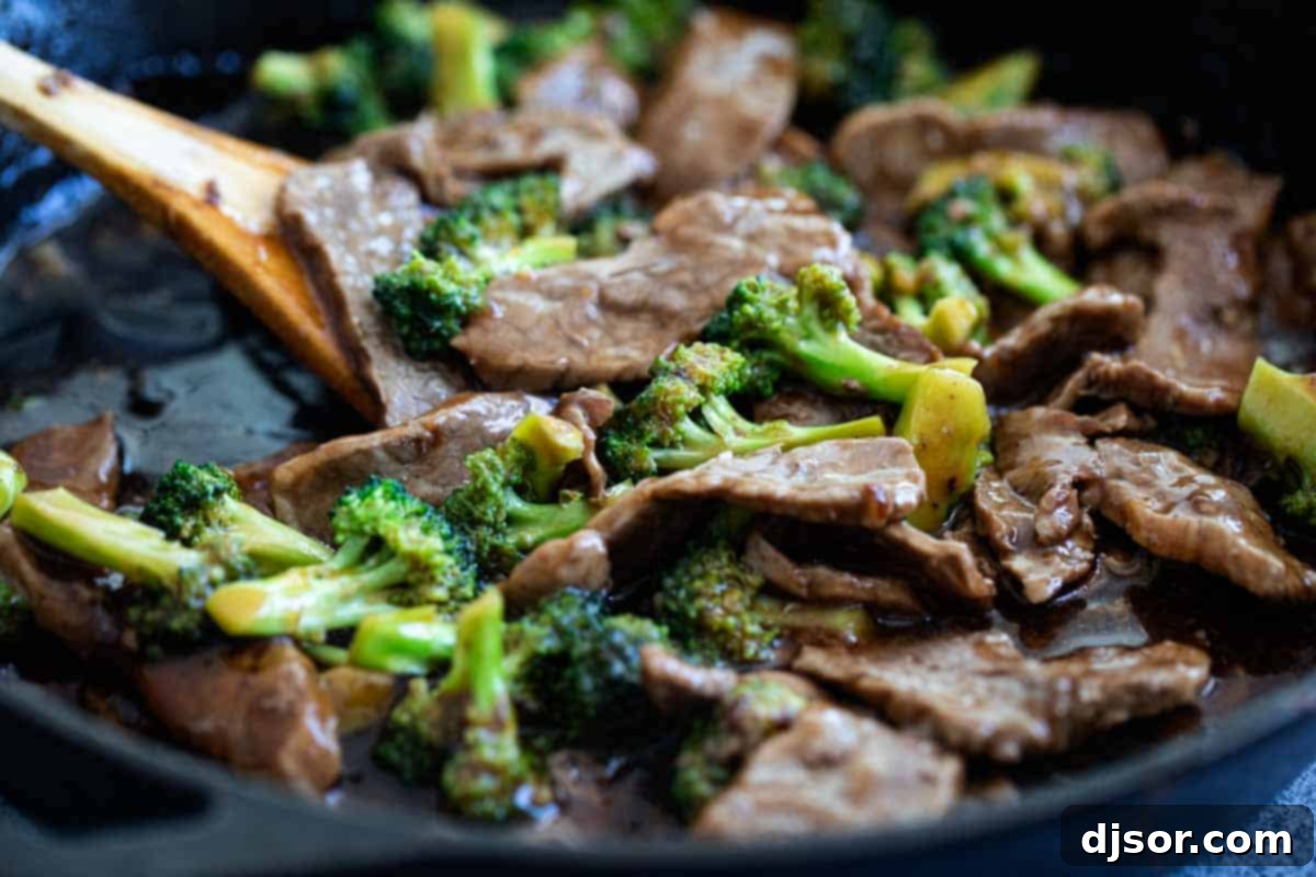 Beef and broccoli being cooked together in a cast iron pan, coated in a rich brown sauce.