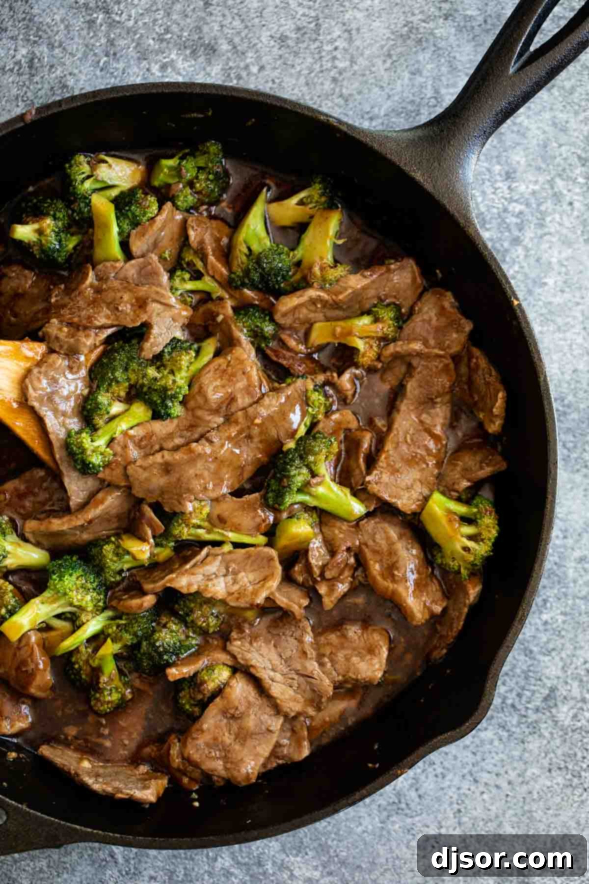 Close-up of beef and broccoli stir-fry in a cast iron pan, coated in a thick, savory sauce.