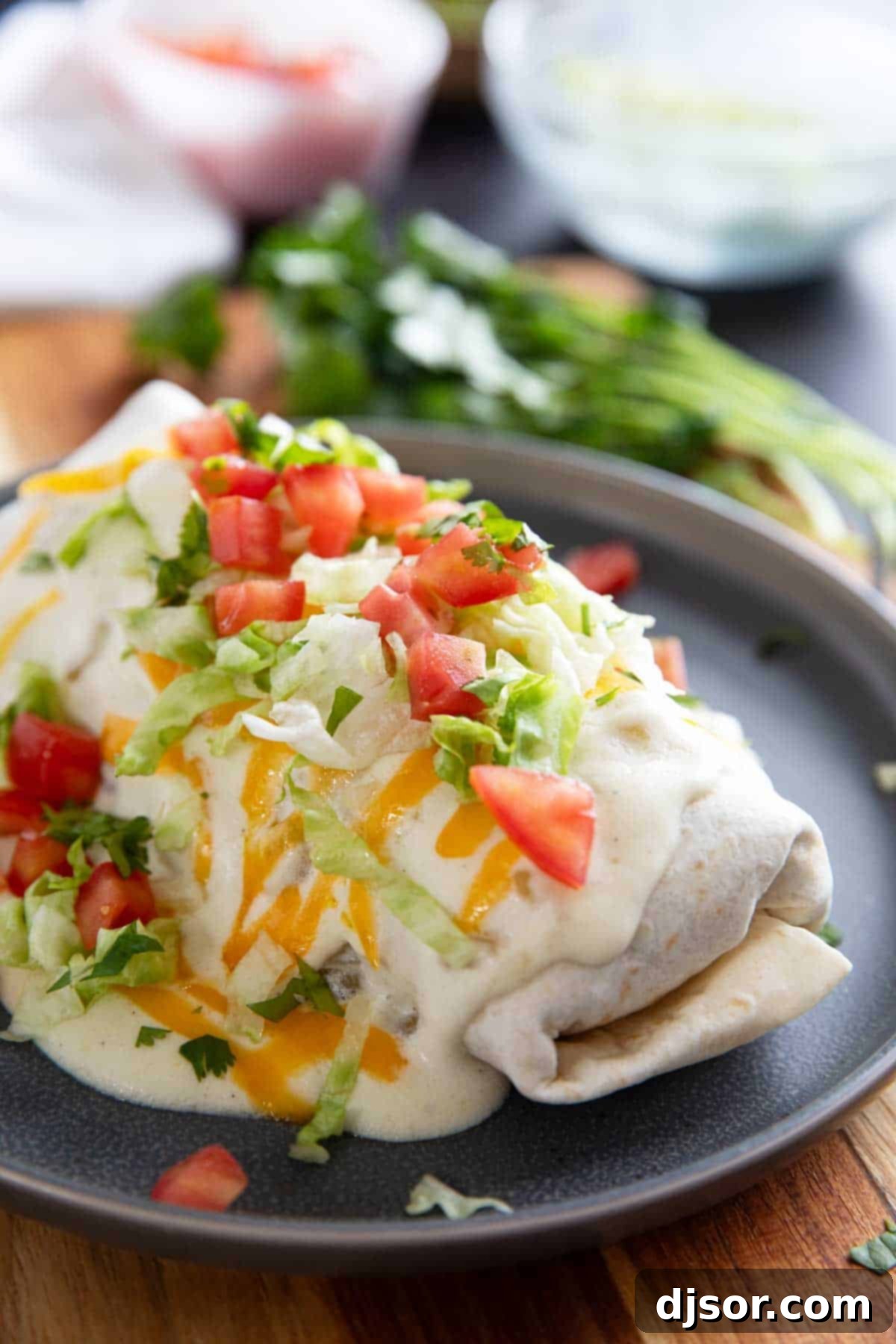 Delicious Smothered Burritos with seasoned ground beef and refried beans, generously covered in a creamy green chile sauce, melted cheese, fresh tomatoes, and crisp lettuce.
