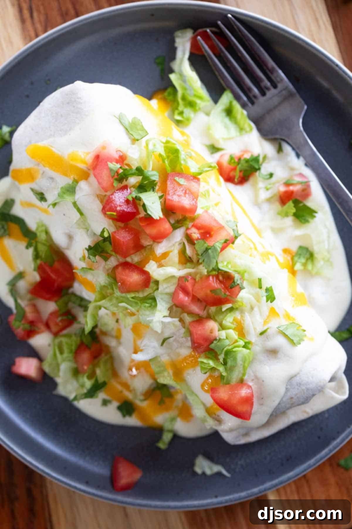 A fully prepared Smothered Burrito, generously covered in creamy green chile sauce, melted cheese, fresh diced tomatoes, and shredded lettuce, ready to be enjoyed.