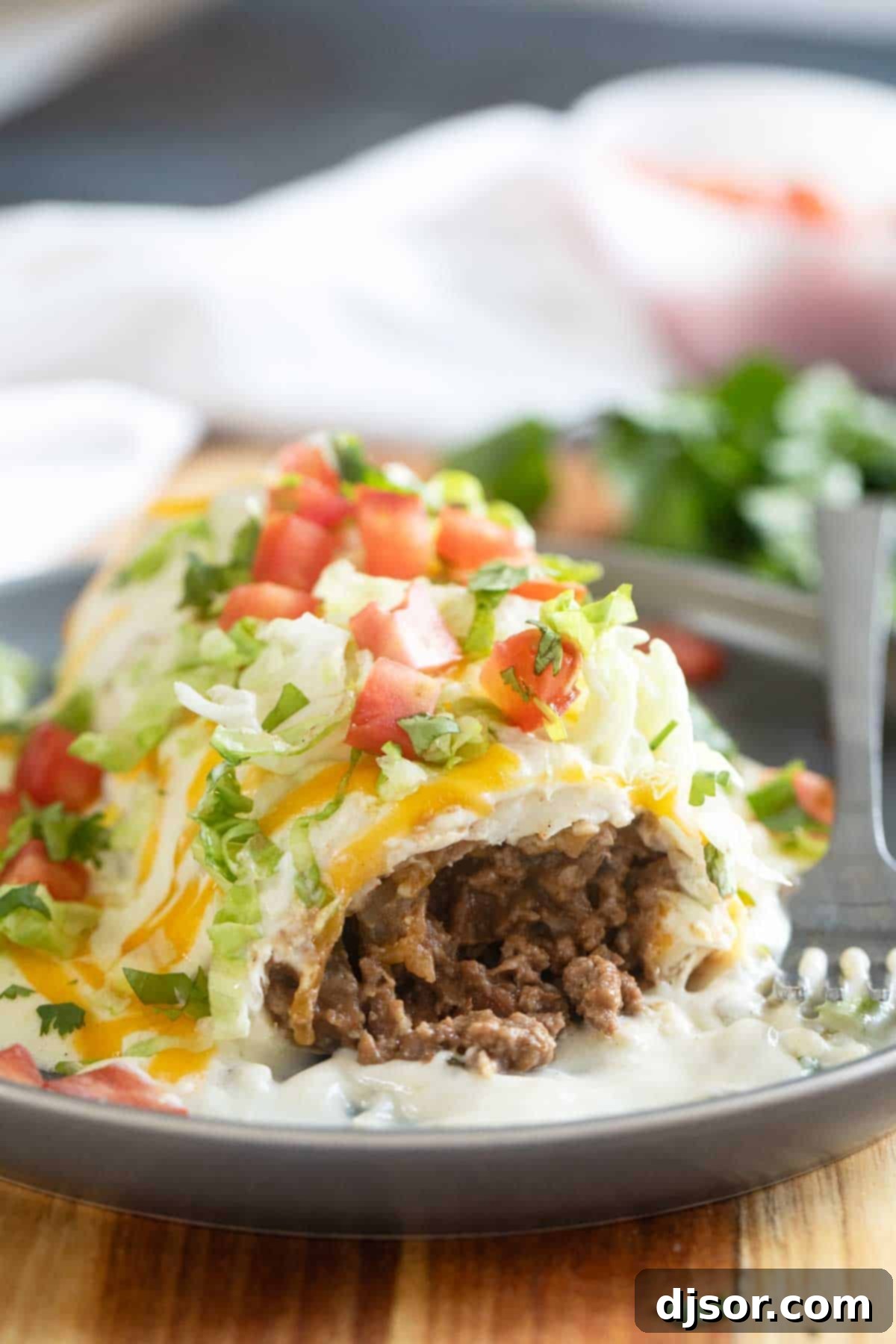 A close-up of a Smothered Burrito with Green Chile Sauce, showing a bite taken out to reveal the savory ground beef and bean filling inside.