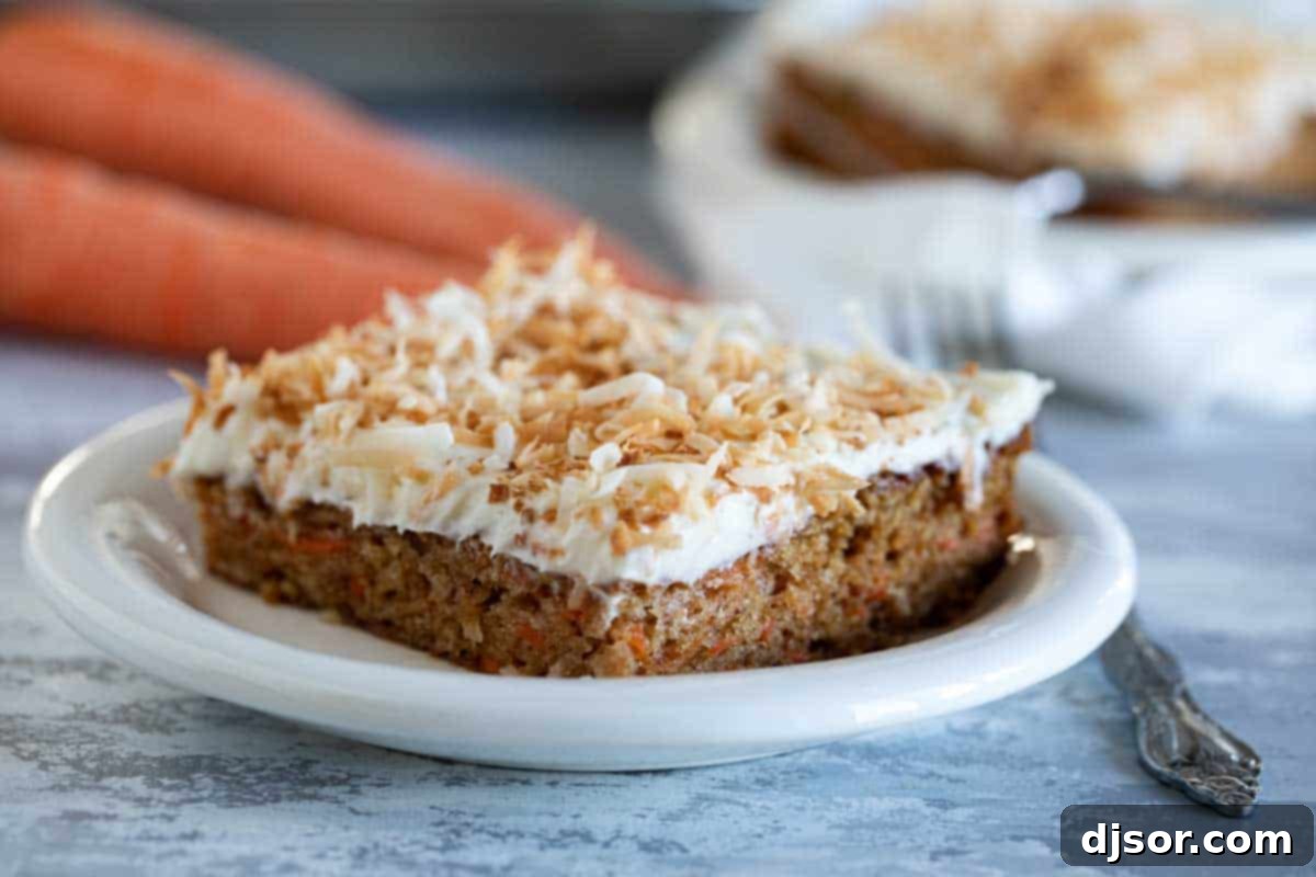 A perfectly moist slice of carrot sheet cake adorned with creamy white frosting and golden toasted coconut flakes, served on a plate with fresh carrots in the background.