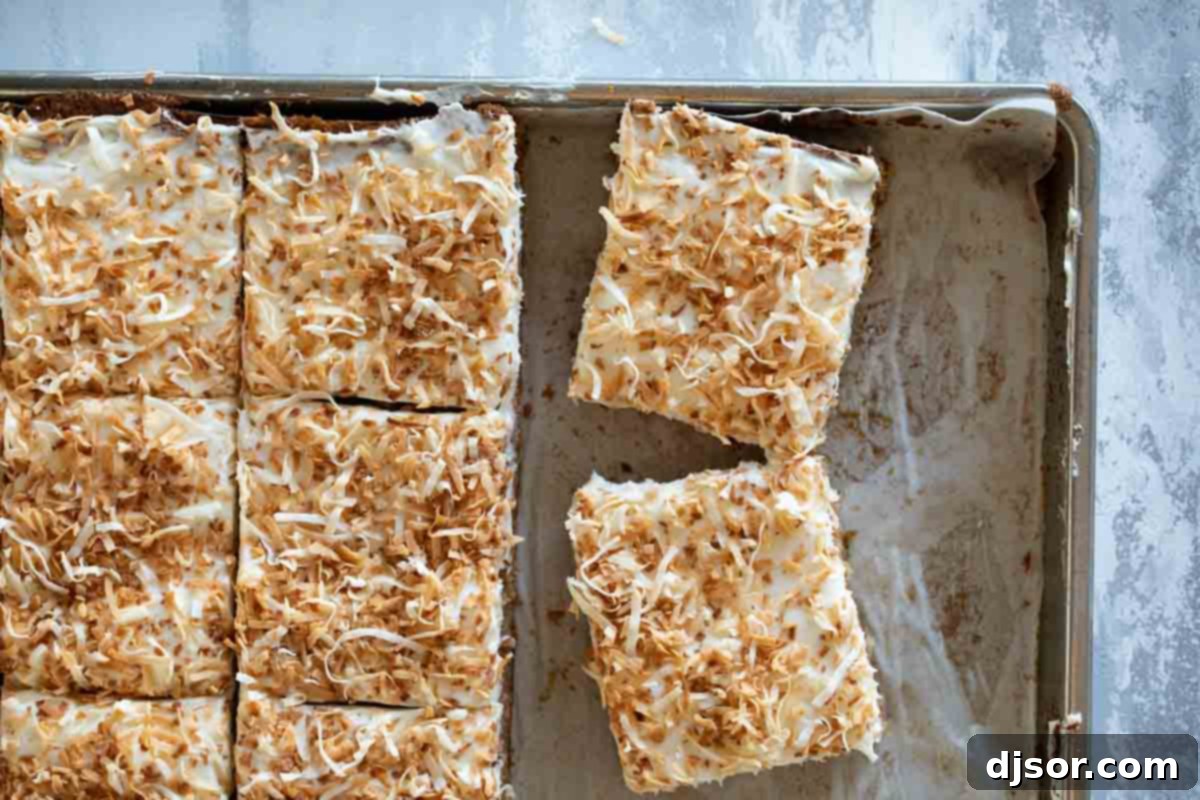 A delectable carrot sheet cake, expertly frosted and topped with toasted coconut, cut into ready-to-serve squares directly in the baking pan, showcasing its generous portion size.