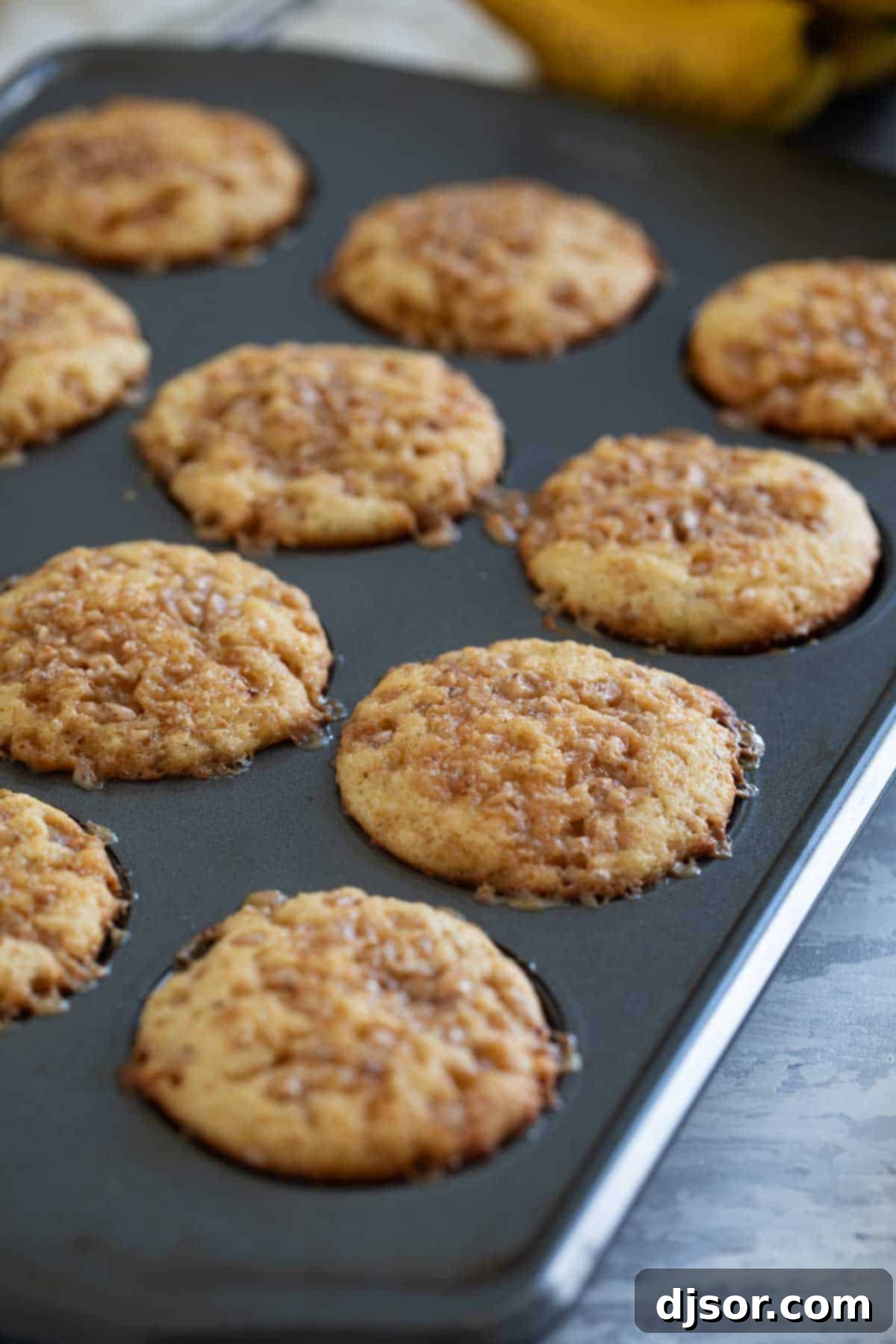 Banana Toffee Treat Muffins 7 Freshly baked Banana Toffee Muffins cooling in a muffin tin, golden brown and topped with melted toffee.