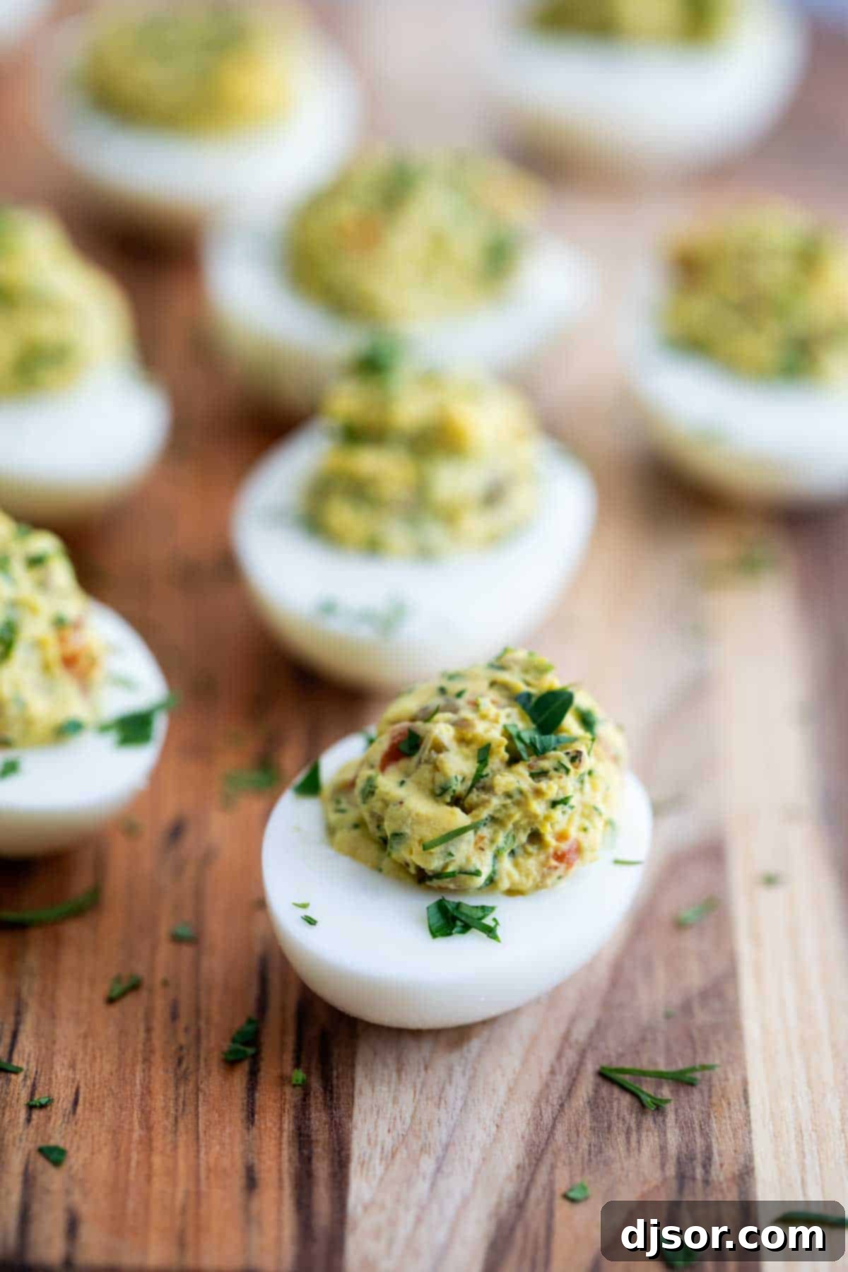 Deviled eggs garnished with green olive slices and fresh herbs, offering a briny and fresh flavor.