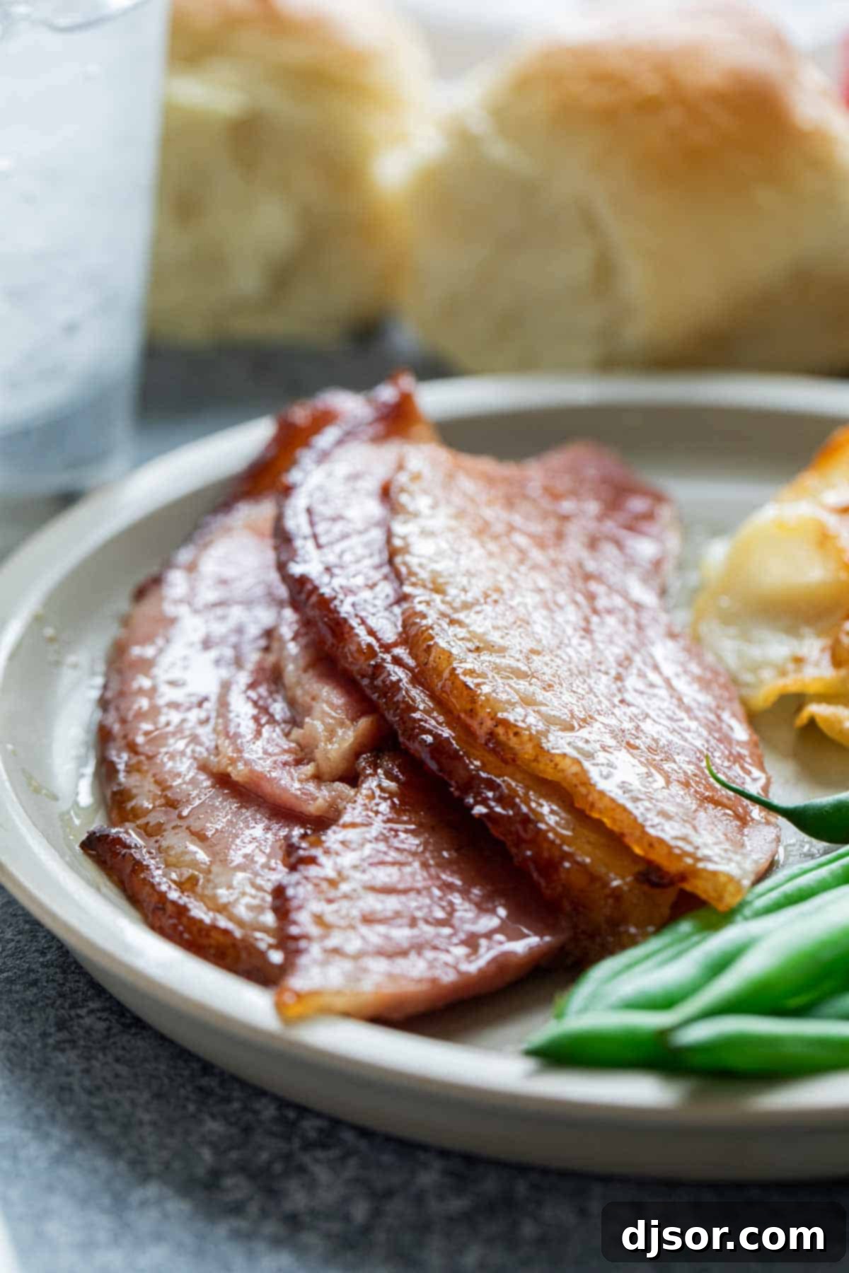 A perfectly cooked slice of Honey Glazed Ham, showcasing its tender meat and caramelized glaze, served on a simple white plate.
