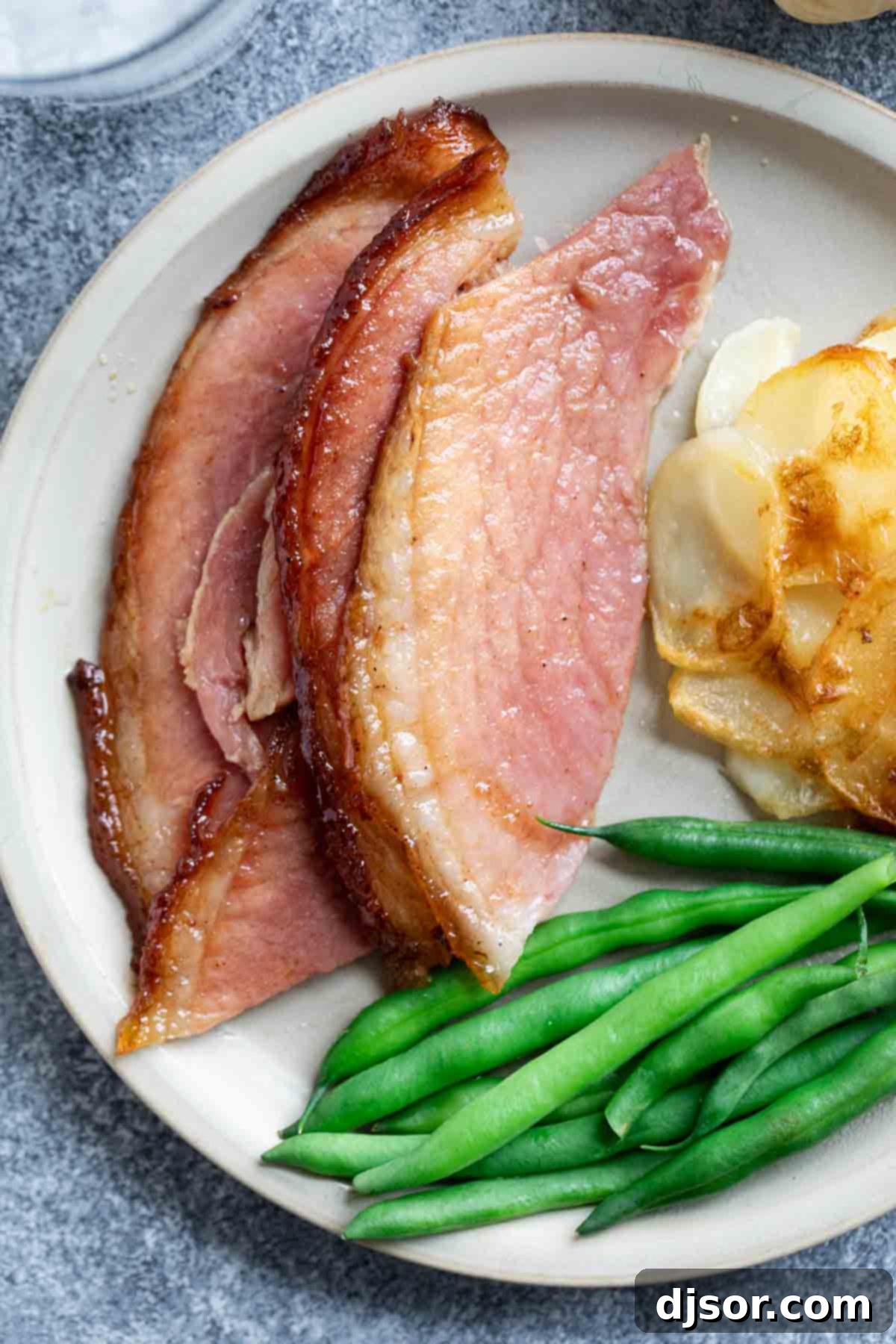 A generous serving of Honey Glazed Ham on a plate, accompanied by vibrant green beans, highlighting a complete and delicious holiday meal.