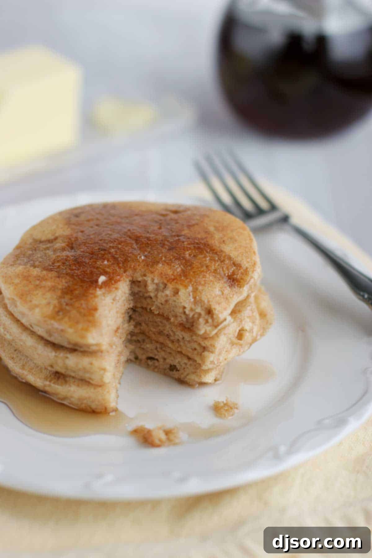 Whole Wheat Blender Pancakes - Use your blender to turn raw whole wheat into pancakes – the perfect breakfast! A stack of golden brown whole wheat blender pancakes, one with a bite taken out, resting on a plate and drizzled with syrup.