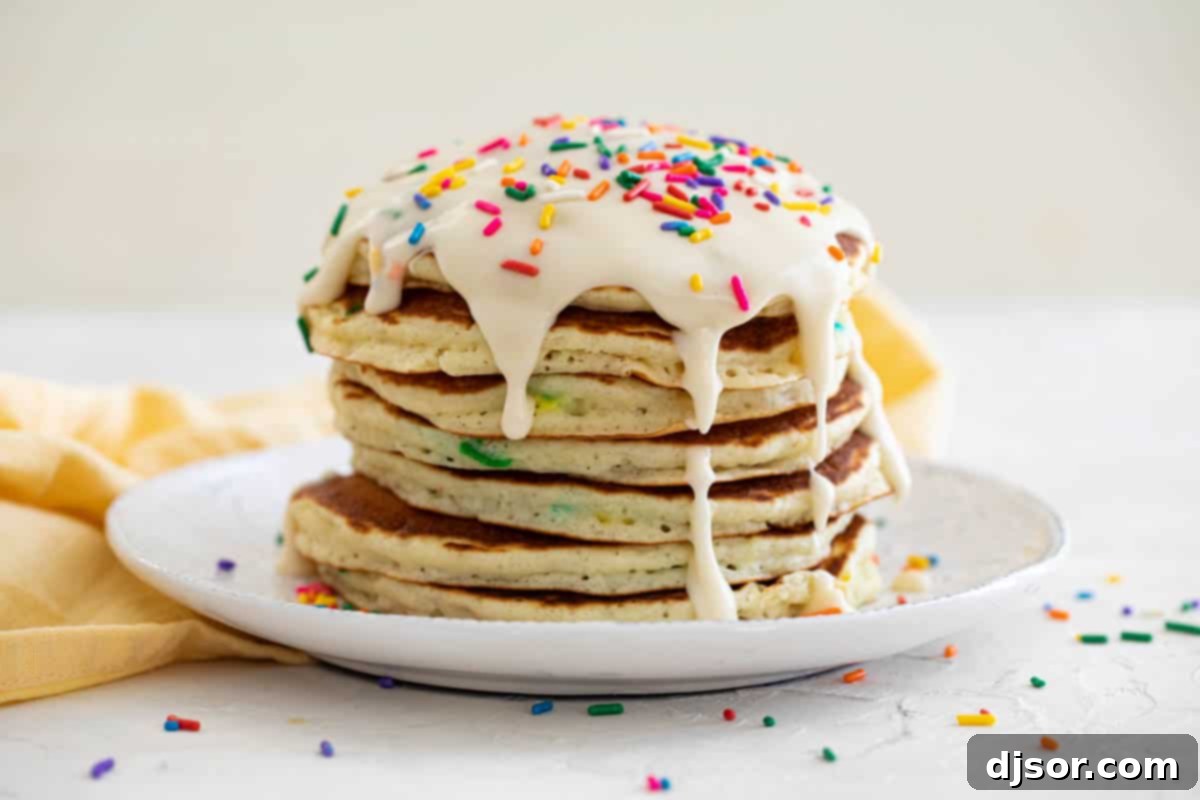 A stack of golden Funfetti Pancakes drizzled with frosting and adorned with a generous sprinkle of colorful confetti, ready for a festive breakfast.