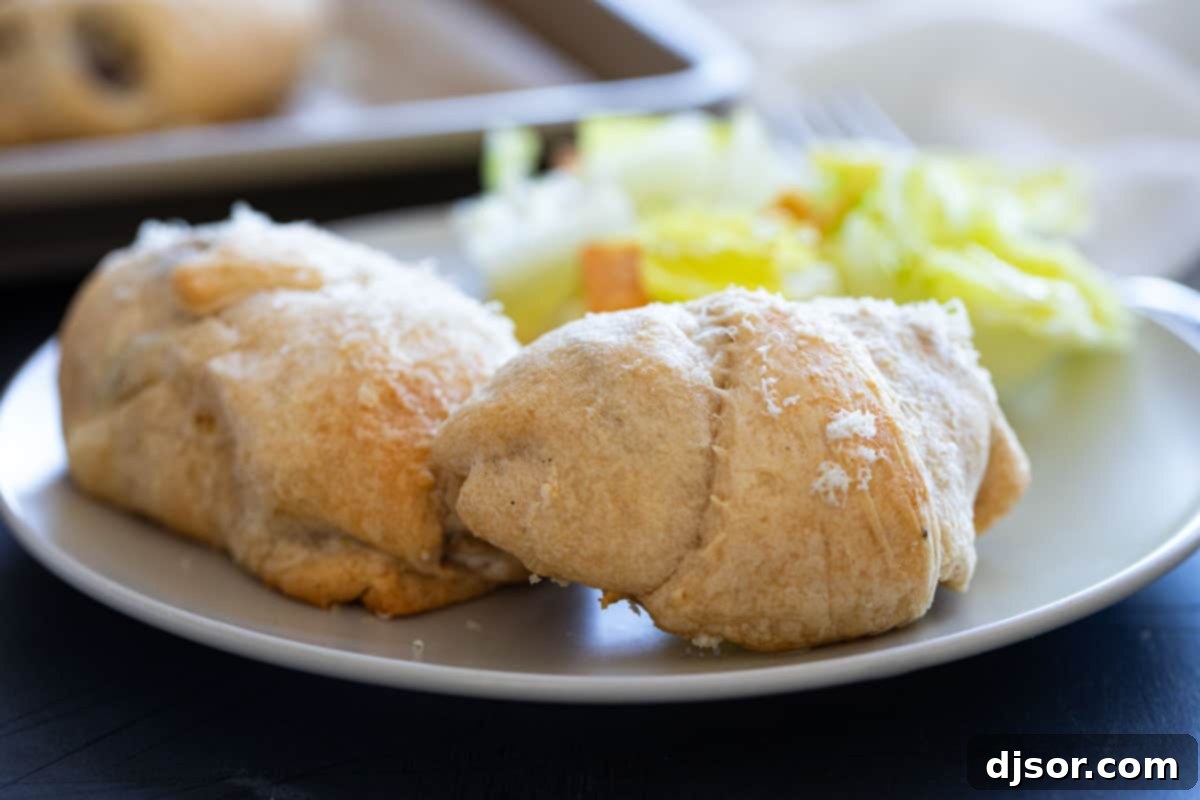Chicken, cream cheese, and mushrooms are rolled and baked inside crescent rolls for these easy, family favorite Chicken Crescent Rolls. Two chicken crescent rolls on a plate with salad.