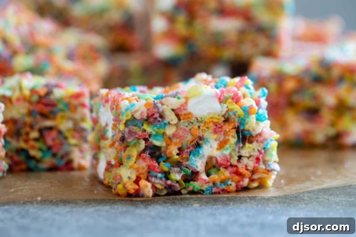 Colorful Fruity Pebble Rice Crispy Treats, cut into perfect squares, resting on parchment paper.