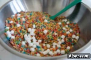 Mixing together fruity pebbles, Rice Krispies, and mini marshmallows in a bowl.