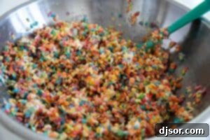 Melted marshmallow mixture being poured over the dry cereal mix for Fruity Pebble Rice Crispy Treats.