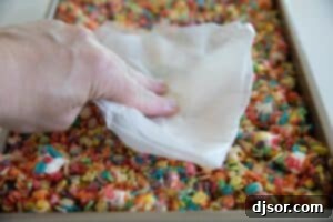 Cereal treats being pressed into a baking pan with wax paper to create an even layer.