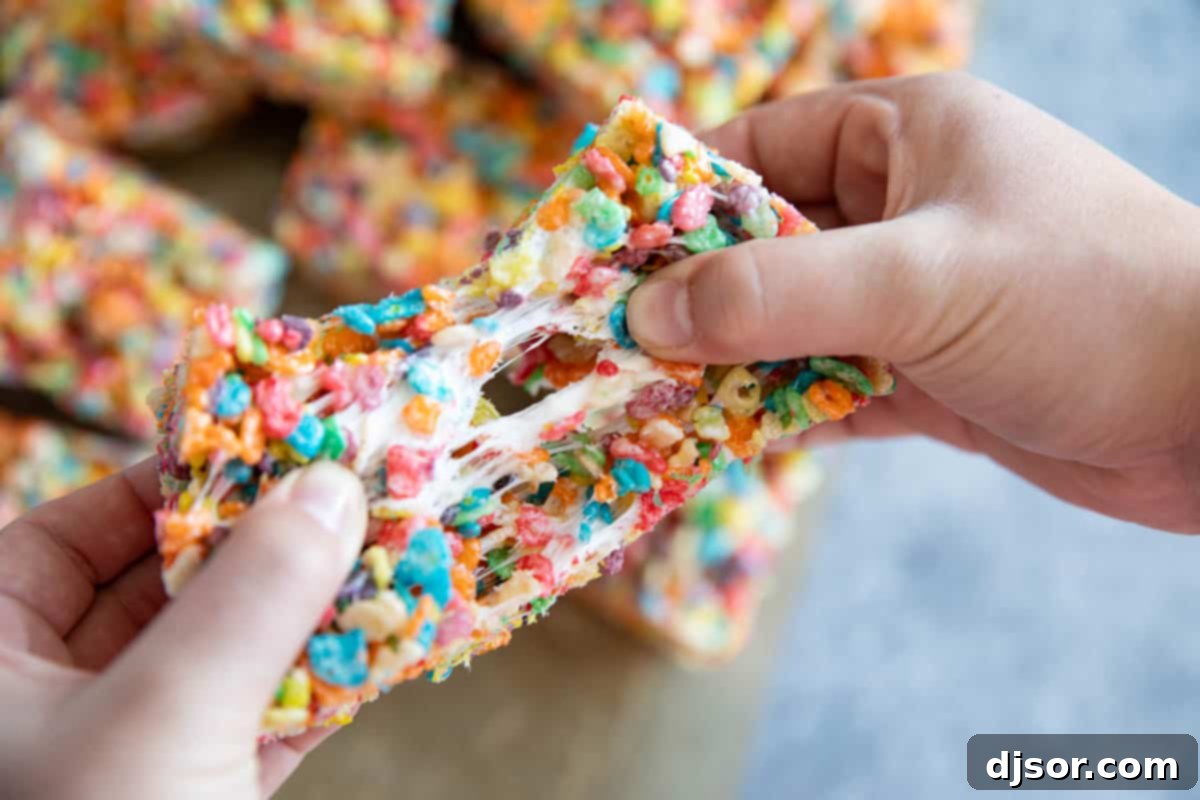 A close-up shot of a Fruity Pebble Rice Crispy Treat being pulled apart, showcasing the gooey, stretchy marshmallows.