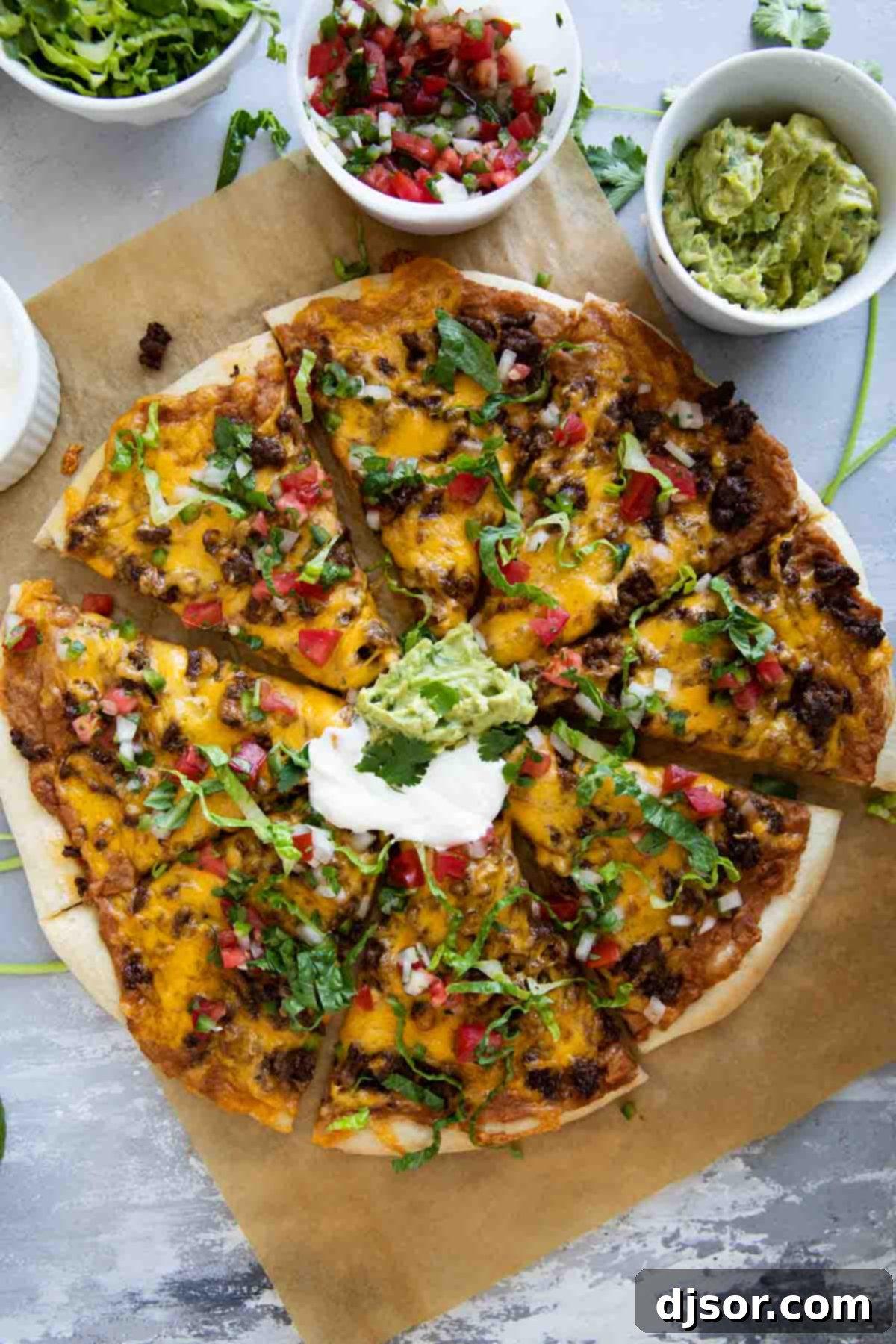 Full taco pizza topped with sour cream, guacamole, lettuce, and pico de gallo.