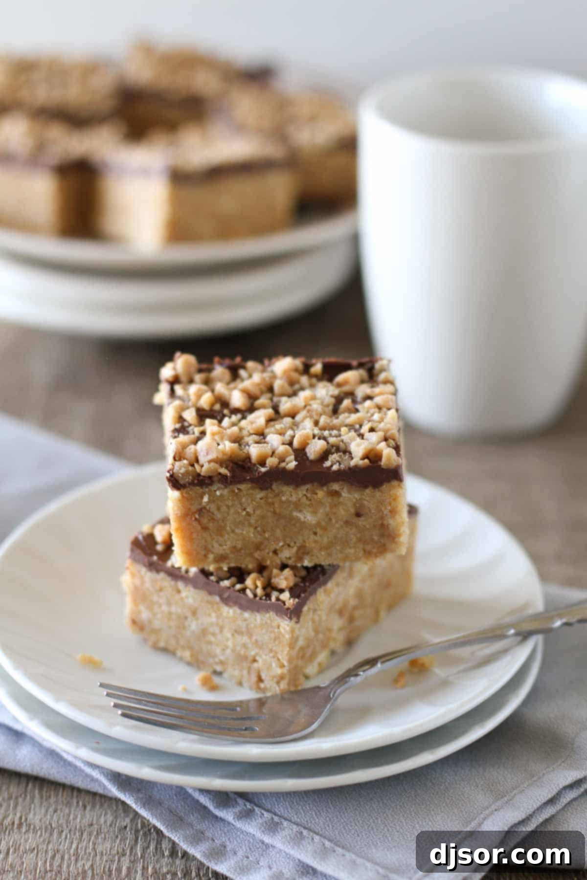 Four ingredient Skor Squares stacked on a pristine white plate, with more delicious bars visible behind, inviting you to try this simple dessert.