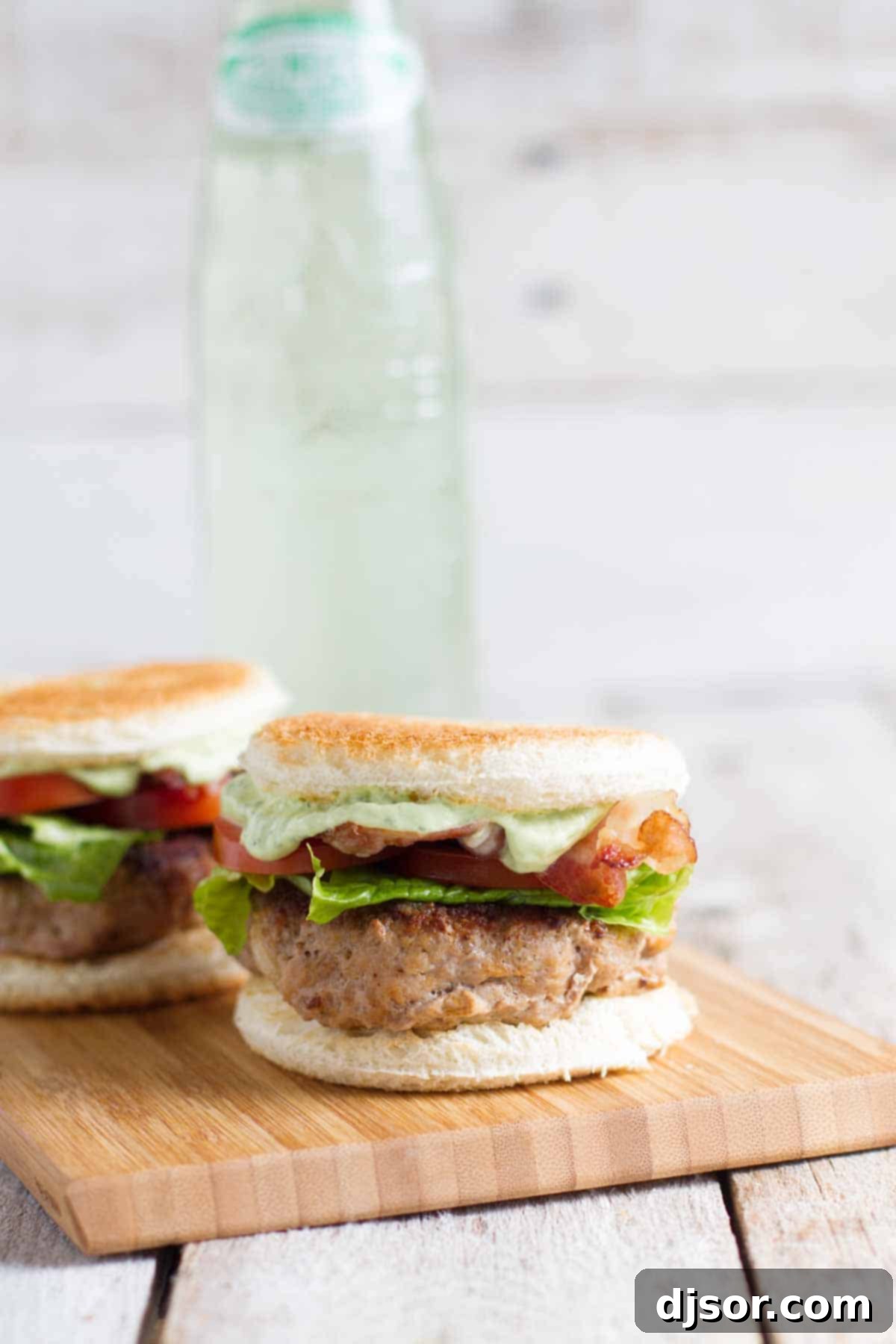 Two Club Burger Sliders with Avocado-Ranch Dressing served on a cutting board with a refreshing drink in the background