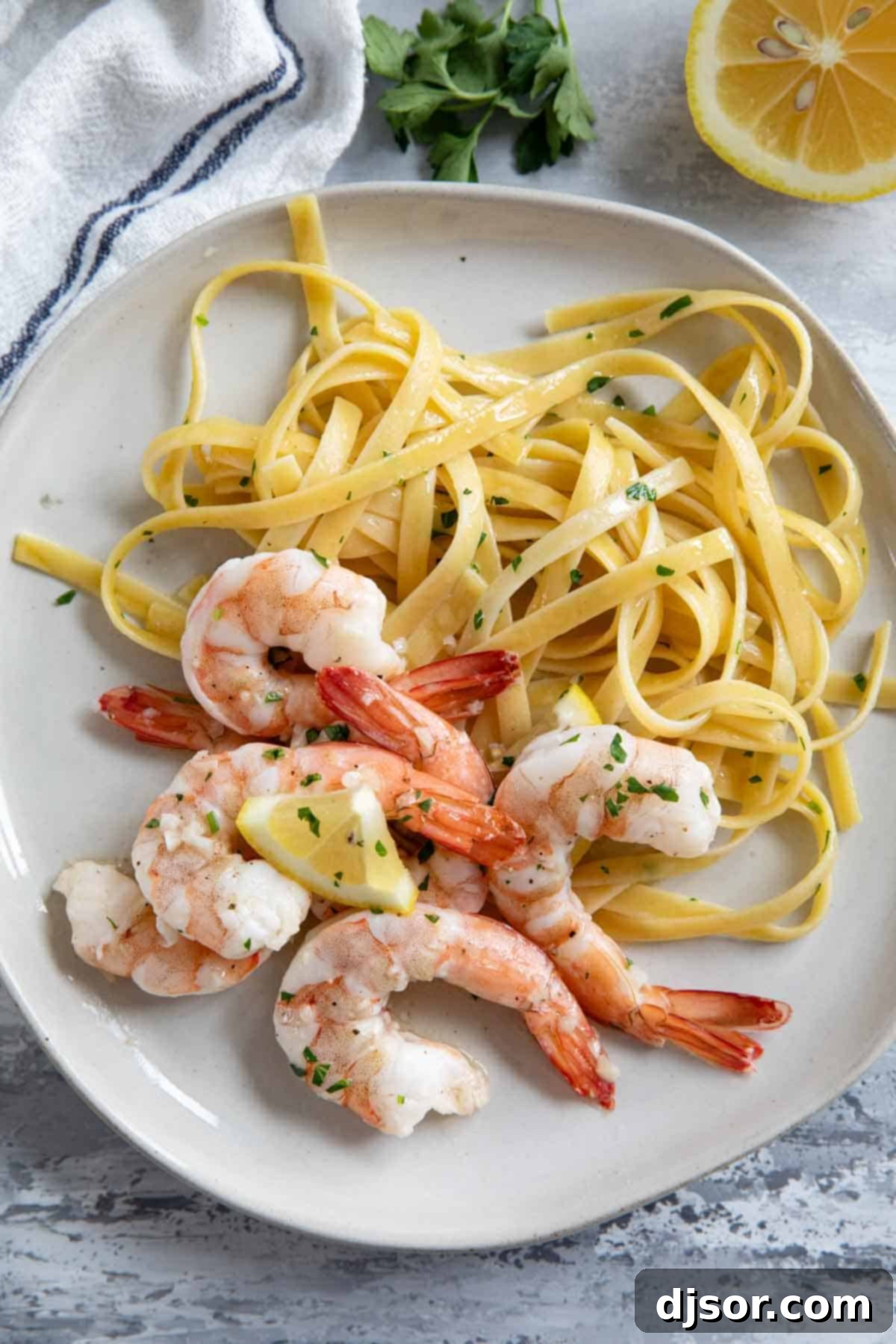 Lemon Garlic Baked Shrimp 7 Baked shrimp served over a bed of pasta on a white plate, garnished with fresh parsley and a lemon wedge.