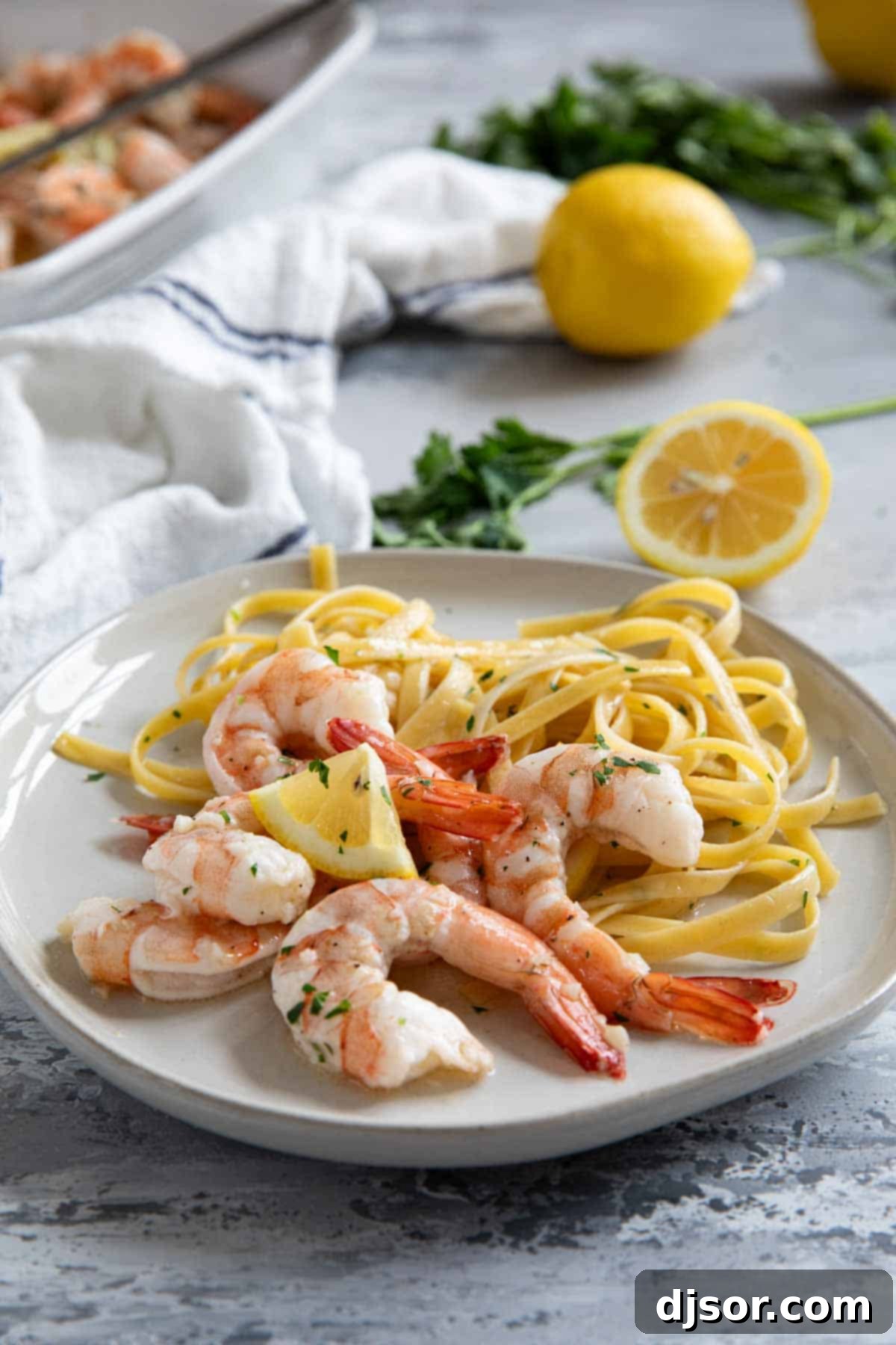 Lemon Garlic Baked Shrimp 8 A plate of linguine topped with baked shrimp, garnished with a lemon slice and fresh herbs, ready to be enjoyed.