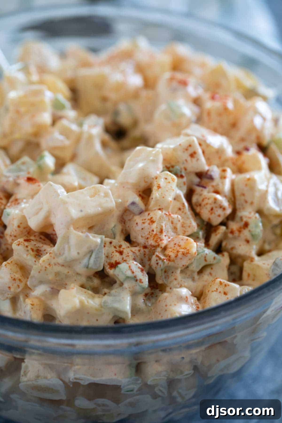 Classic Creamy Potato Salad 9 A large, inviting glass bowl of classic potato salad, generously sprinkled with smoked paprika and fresh green herbs for a pop of color. The creamy texture and appealing presentation make it an ideal side dish, ready to be served and enjoyed at any gathering.