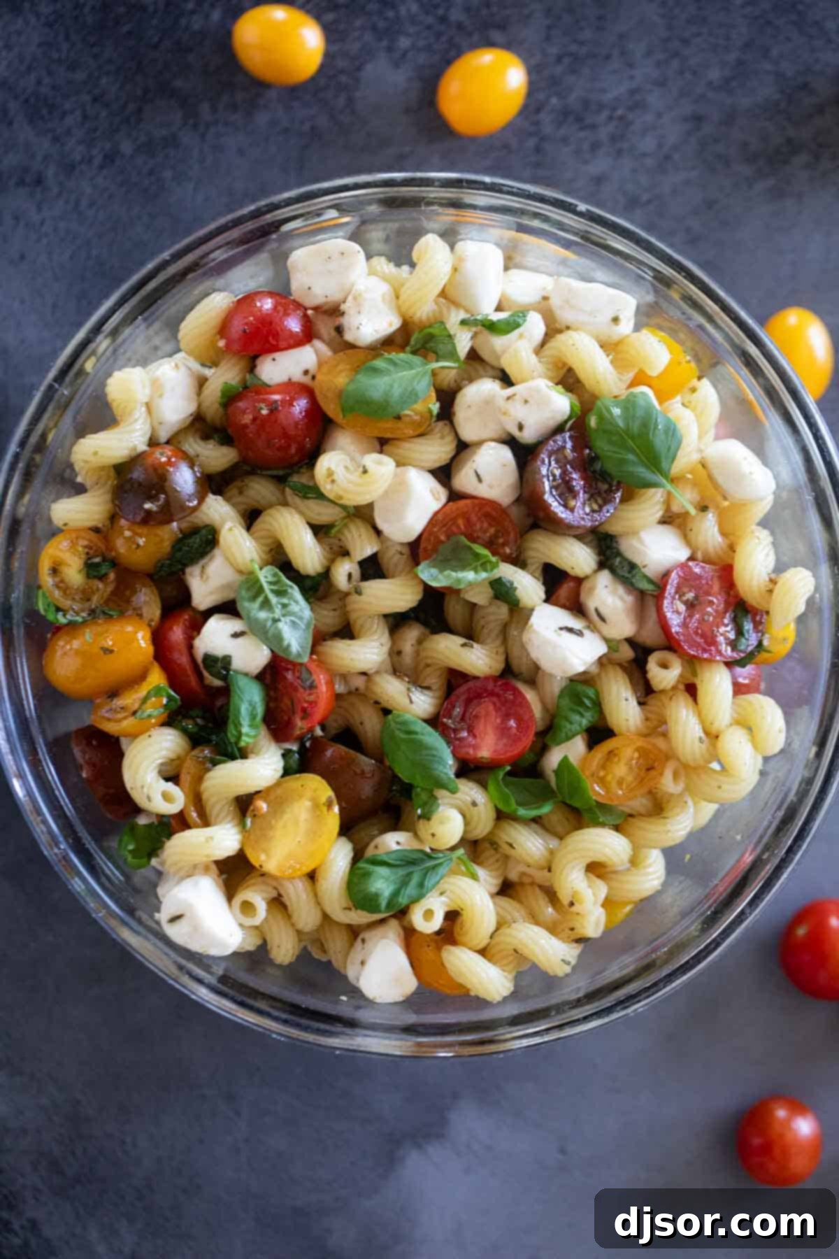 A large bowl generously filled with Caprese Pasta Salad, showcasing the pasta, vibrant red tomatoes, creamy white mozzarella, and fresh green basil leaves.