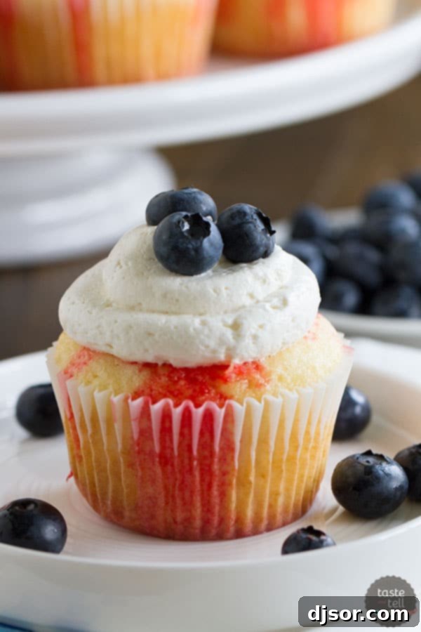 Jiggly Jell-O Poke Cupcakes 2 Vibrantly patriotic Jello poke cupcakes, showcasing red Jello stripes, white frosting, and fresh blue blueberries.