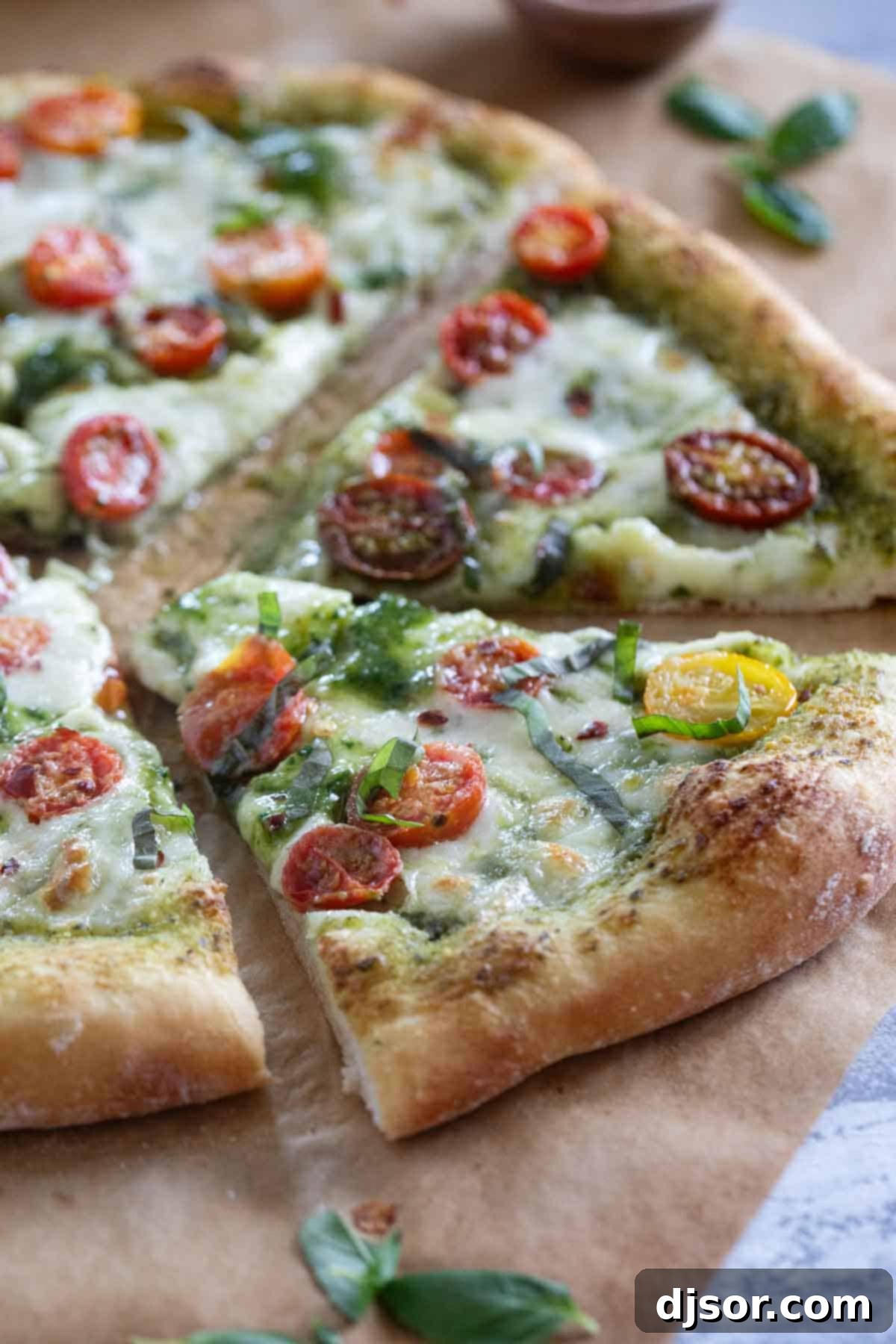 A close-up of a perfectly baked Pesto Pizza, freshly sliced into individual wedges, generously garnished with vibrant fresh basil leaves, and displaying a perfectly golden, crispy crust and melted, bubbly mozzarella cheese. It's ready to be picked up and savored.