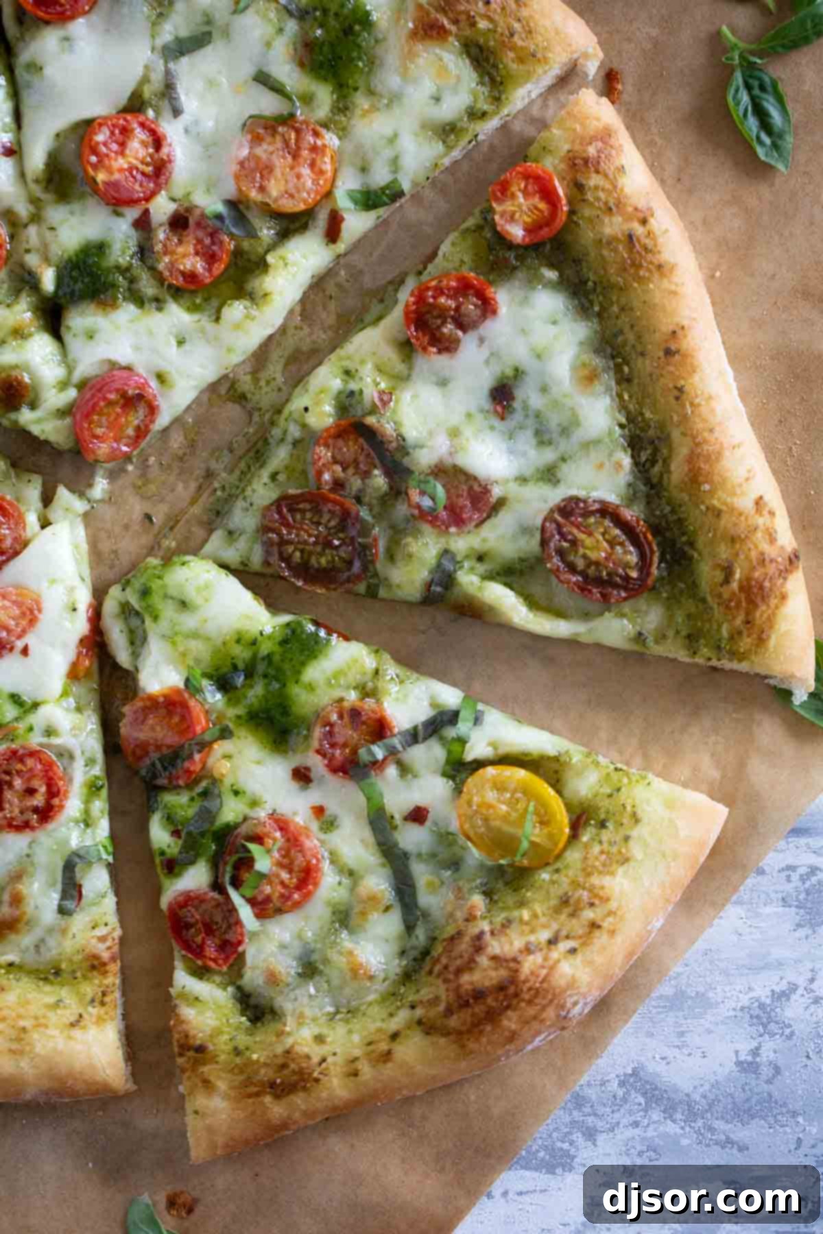 A single, delectable slice of Pesto Pizza, adorned with perfectly roasted cherry tomatoes and fresh basil, positioned against a blurred background of the whole pizza, inviting diners to savor its fresh flavors.