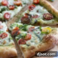 Pesto Pizza with tomatoes and fresh basil cut into slices.