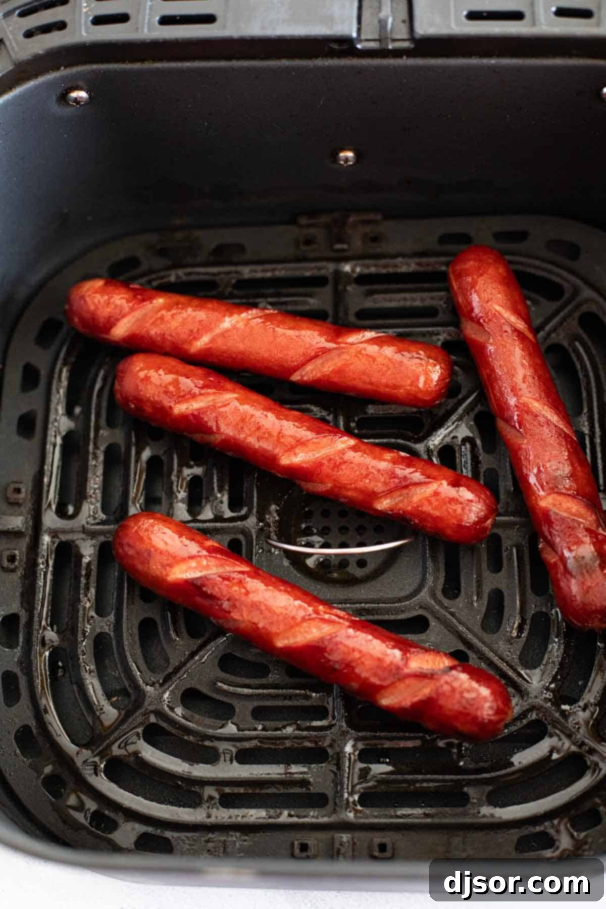 Cooked hot dogs in an air fryer basket.