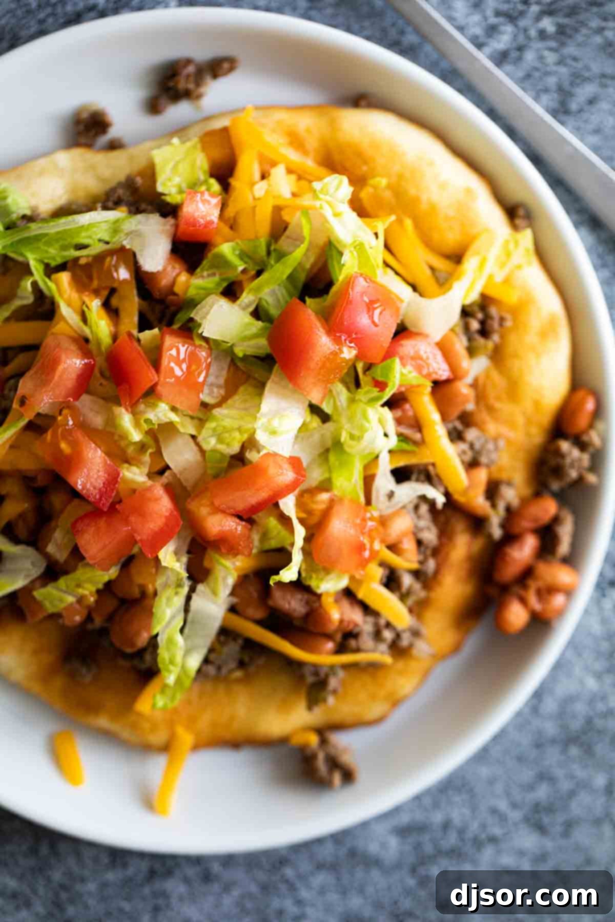 A magnificent Navajo Taco, generously loaded with seasoned ground beef, beans, and fresh vibrant toppings, ready to be enjoyed. Overhead shot of a fully assembled Navajo Taco, brimming with fresh and savory toppings