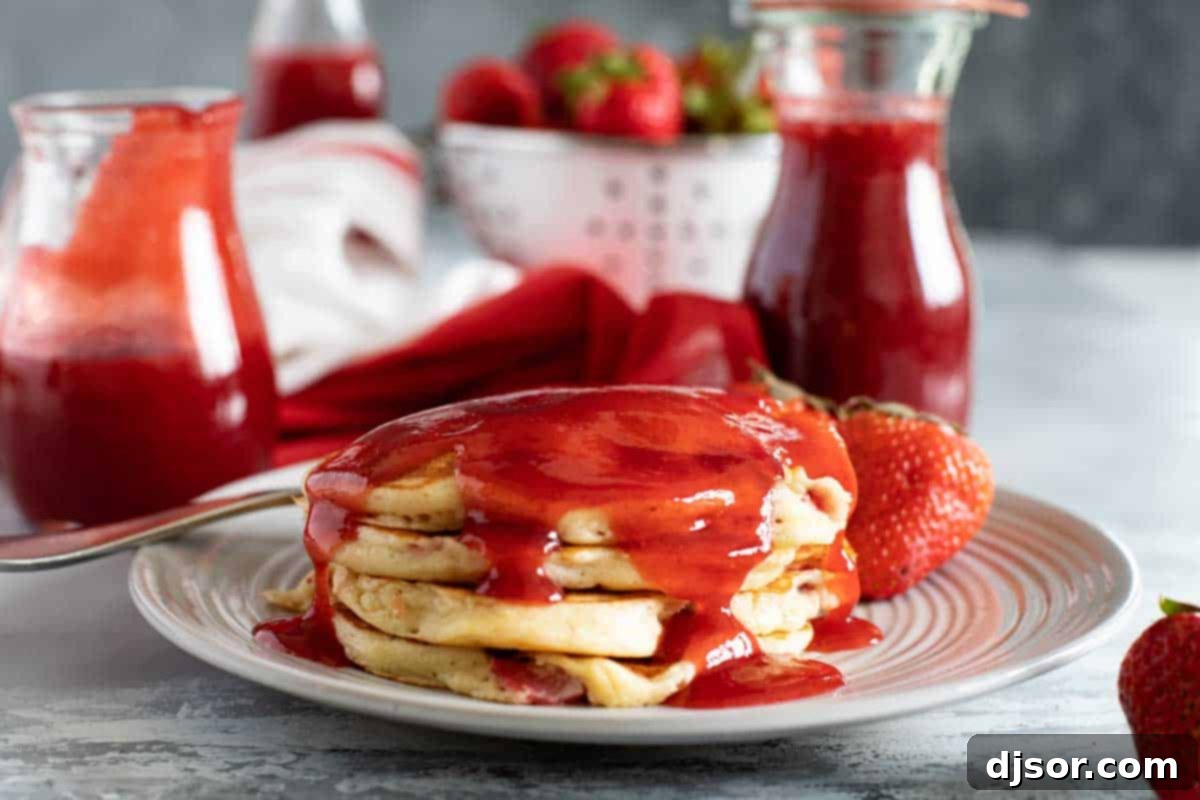 A stack of golden brown strawberry pancakes on a white plate, drizzled with strawberry syrup and garnished with fresh strawberry slices, ready to be enjoyed for breakfast.