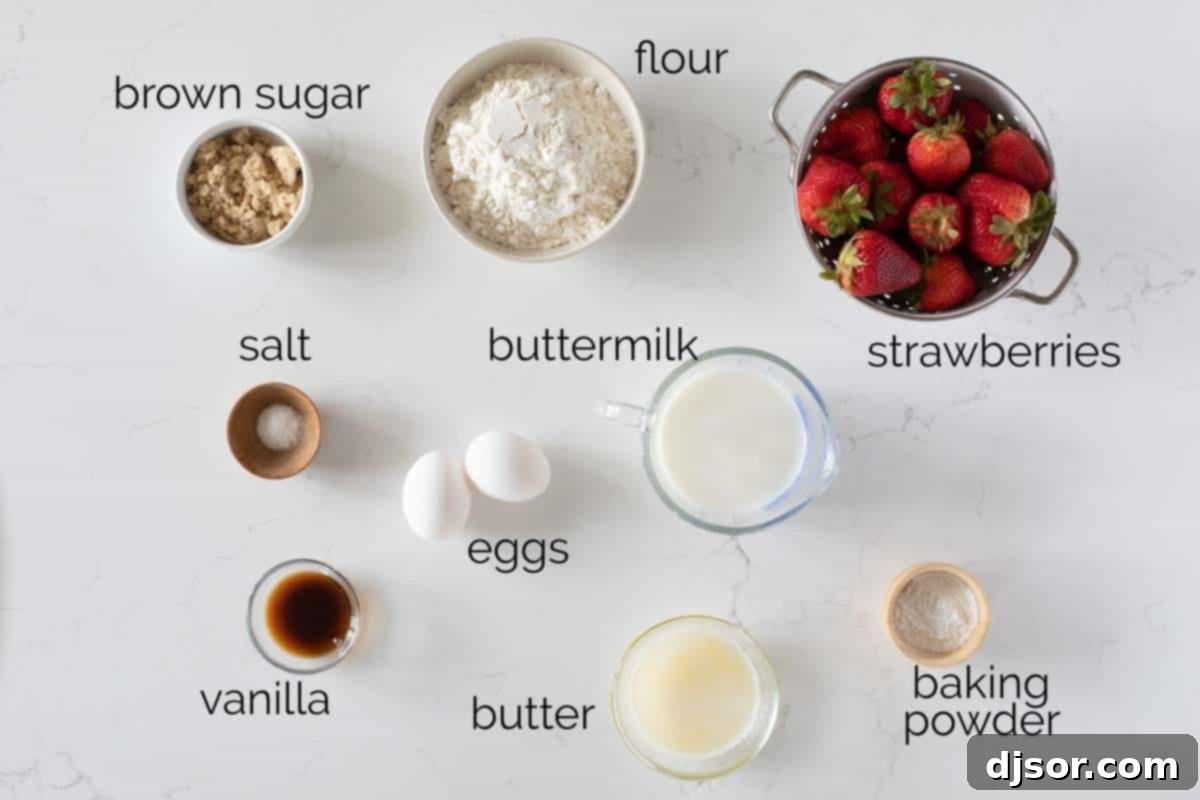 A collection of fresh ingredients laid out on a wooden surface, including all-purpose flour, brown sugar, baking powder, salt, buttermilk, eggs, melted butter, vanilla extract, and ripe strawberries, ready for making strawberry pancakes.