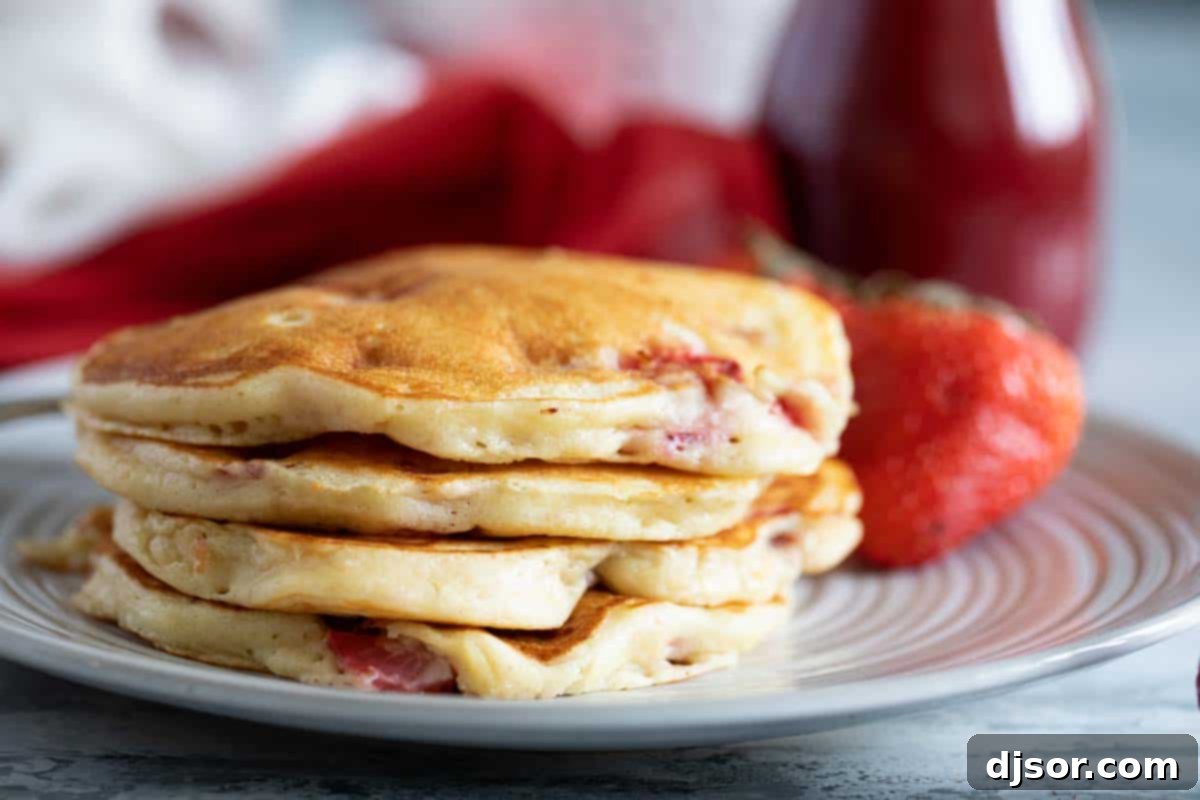 A towering stack of freshly cooked, fluffy strawberry pancakes, perfectly golden brown and ready to be served for breakfast or brunch.