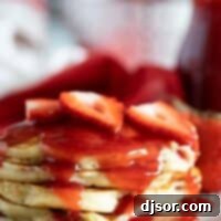 A stack of fluffy strawberry pancakes, generously topped with fresh berries and strawberry syrup, ready for a delightful breakfast or brunch.