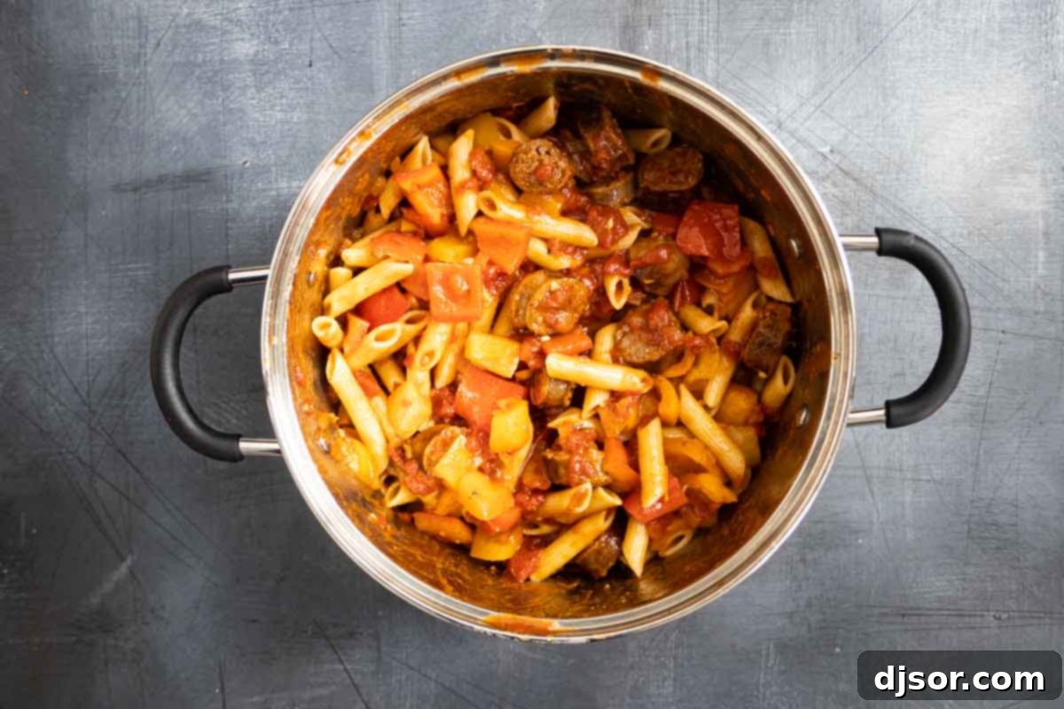The finished Sausage and Peppers Pasta, ready to be served and enjoyed. a large pot filled with cooked pasta, bell peppers, and sliced sausage coated in a rich tomato sauce