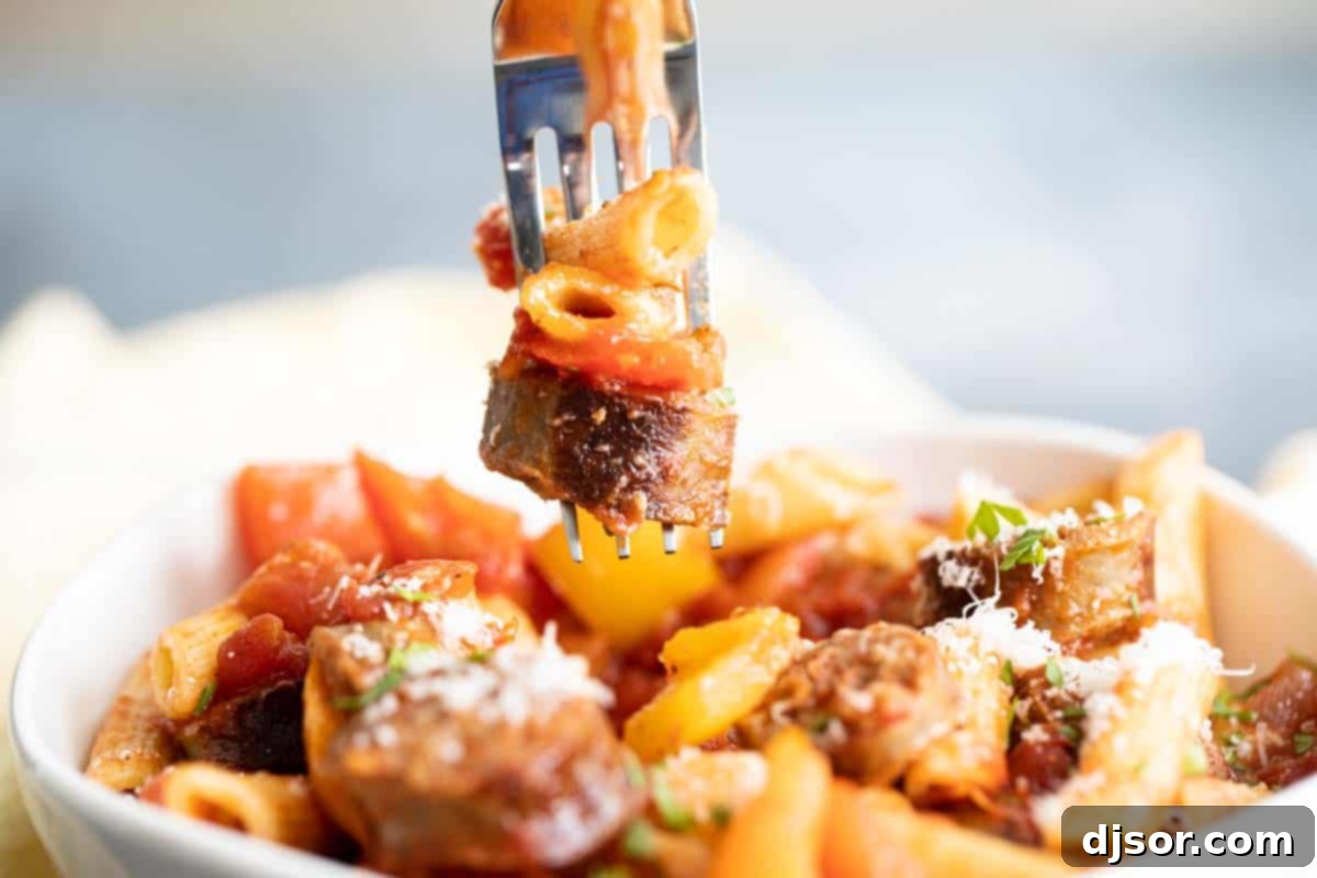 A perfect bite of Sausage and Peppers Pasta, showcasing all the delicious components. a fork lifting a bite of penne pasta with a slice of sausage and bell pepper