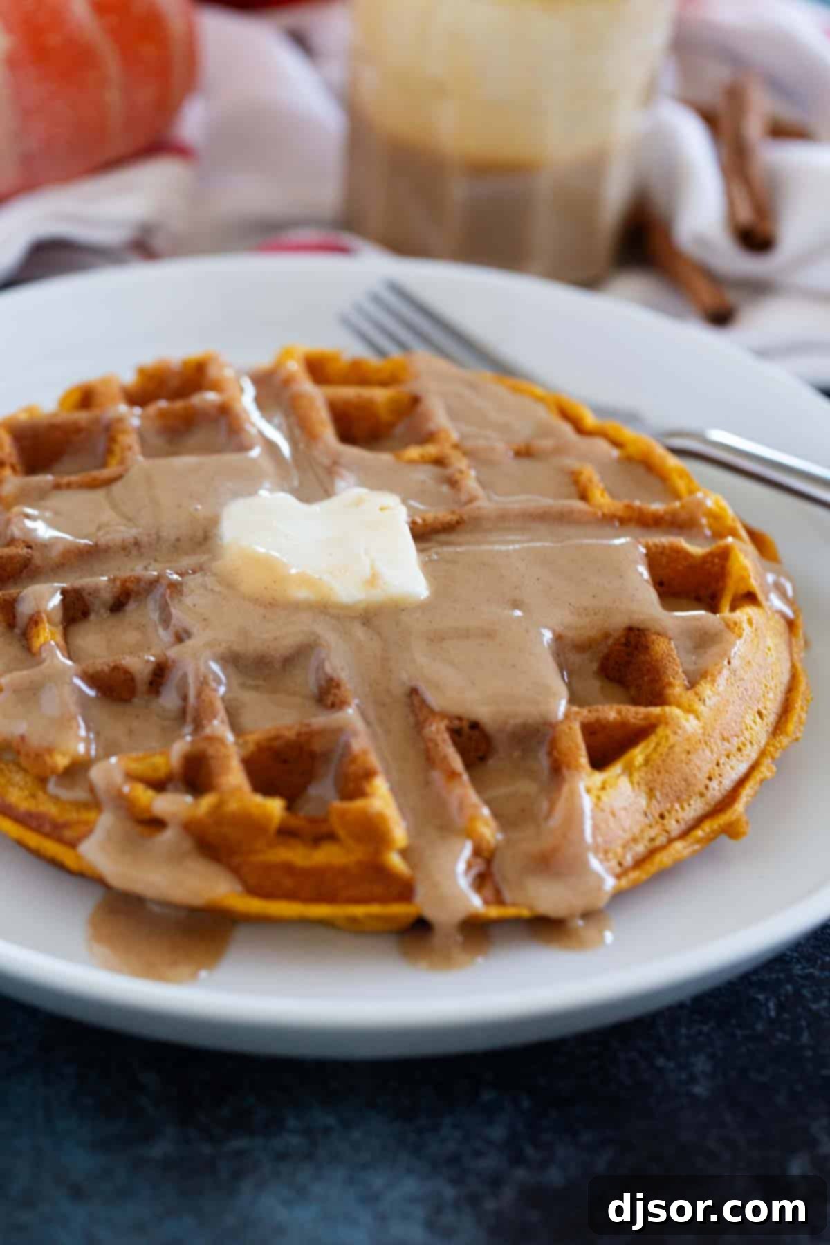 Autumn Pumpkin Waffles 7 A beautifully arranged stack of golden Pumpkin Waffles on a pristine white plate, gracefully drizzled with a sweet and shiny cinnamon syrup.