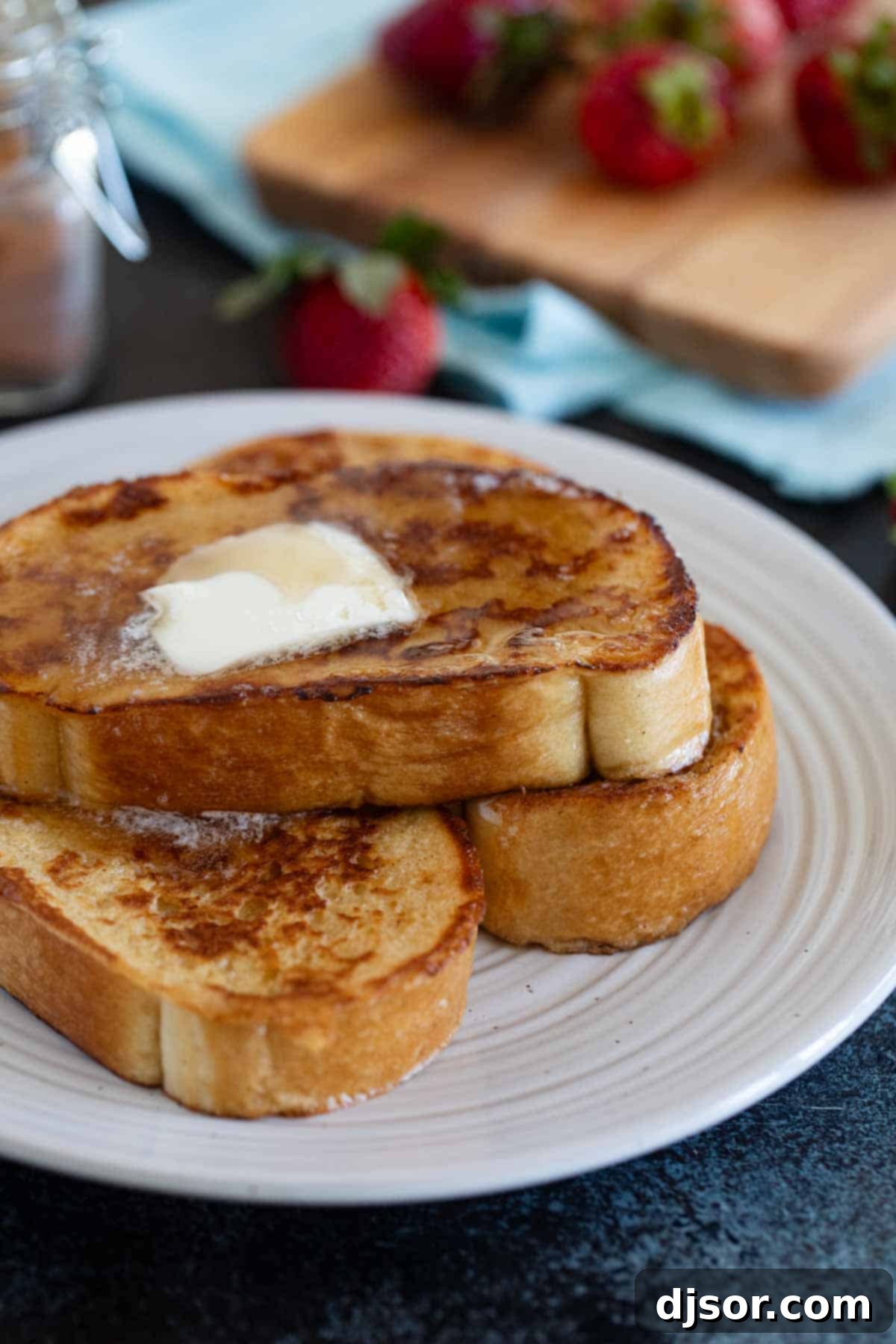 Pain Perdu 7 A stack of golden-brown French Toast slices, generously drizzled with maple syrup and topped with a pat of melting butter.