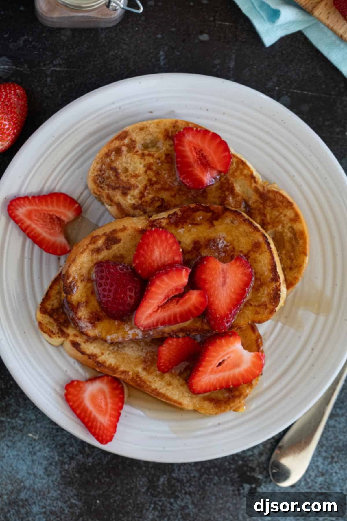 Pain Perdu 8 Two slices of fluffy French Toast artfully arranged on a white plate, garnished with fresh sliced strawberries and a generous drizzle of maple syrup.