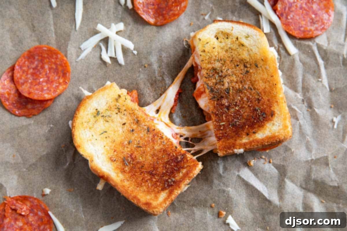 A perfectly golden brown pizza grilled cheese sandwich, cut in half to reveal its melty interior.
