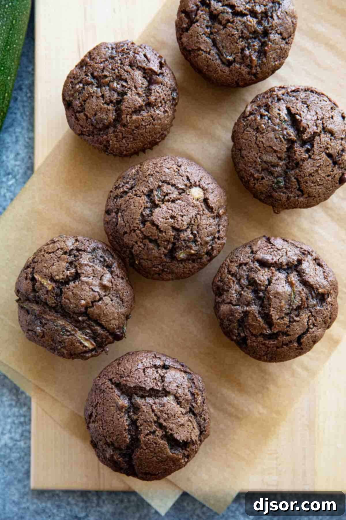 Cooling Down: Freshly Baked Chocolate Zucchini Muffins A batch of warm, freshly baked Chocolate Zucchini Muffins cooling on parchment paper atop a wooden board.