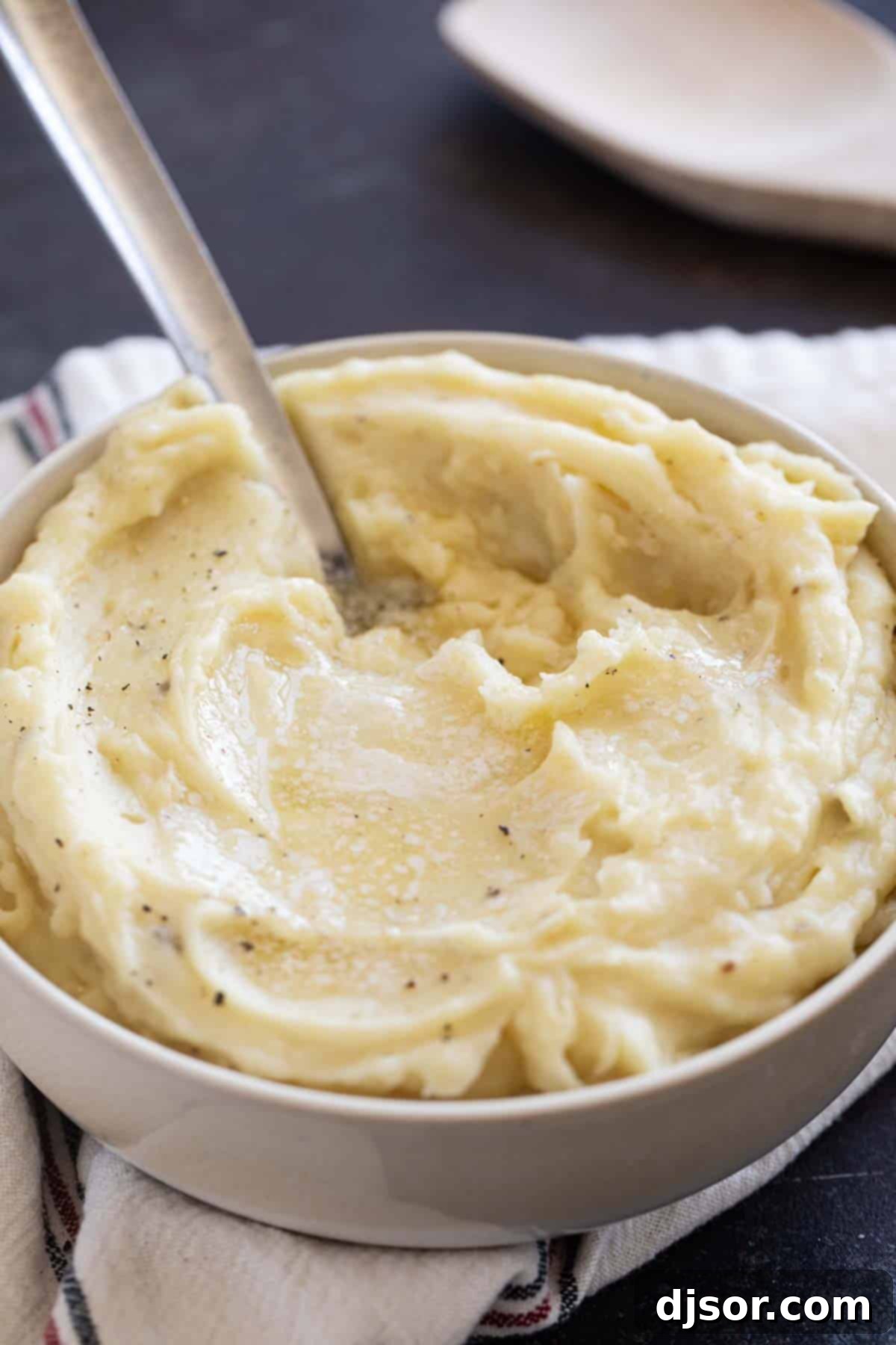 Perfectly Creamy Crockpot Mashed Potatoes 8 A large bowl of crockpot mashed potatoes, adorned with a melting pat of butter and a spoon, inviting guests to serve themselves.